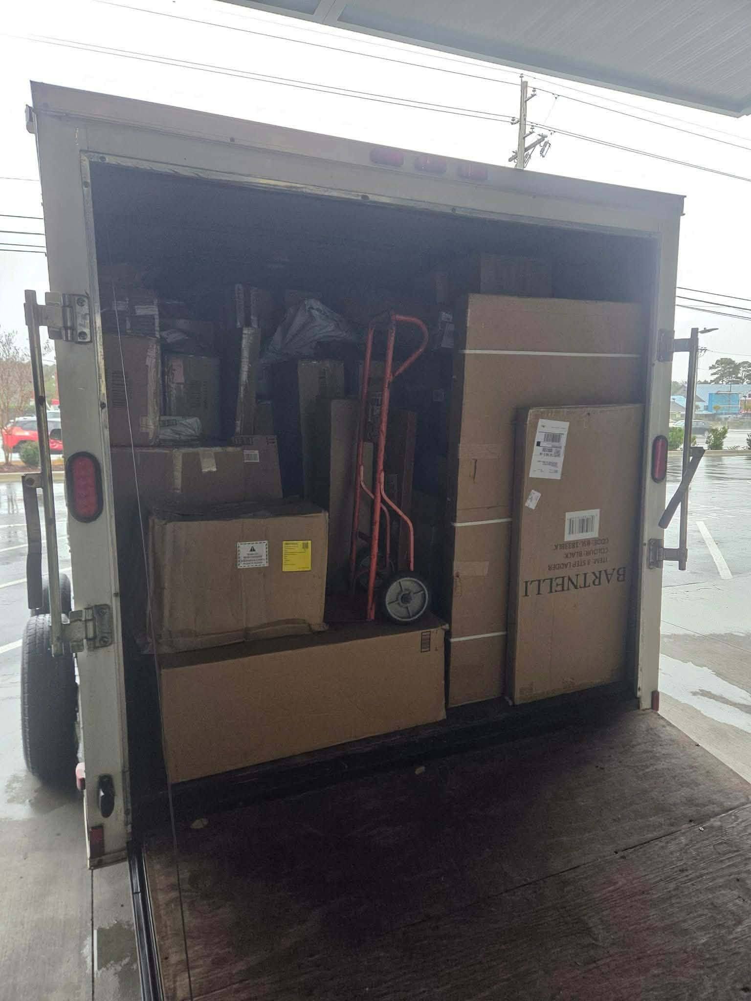 Open truck with a large boxed machine and cables secured inside at a loading area.