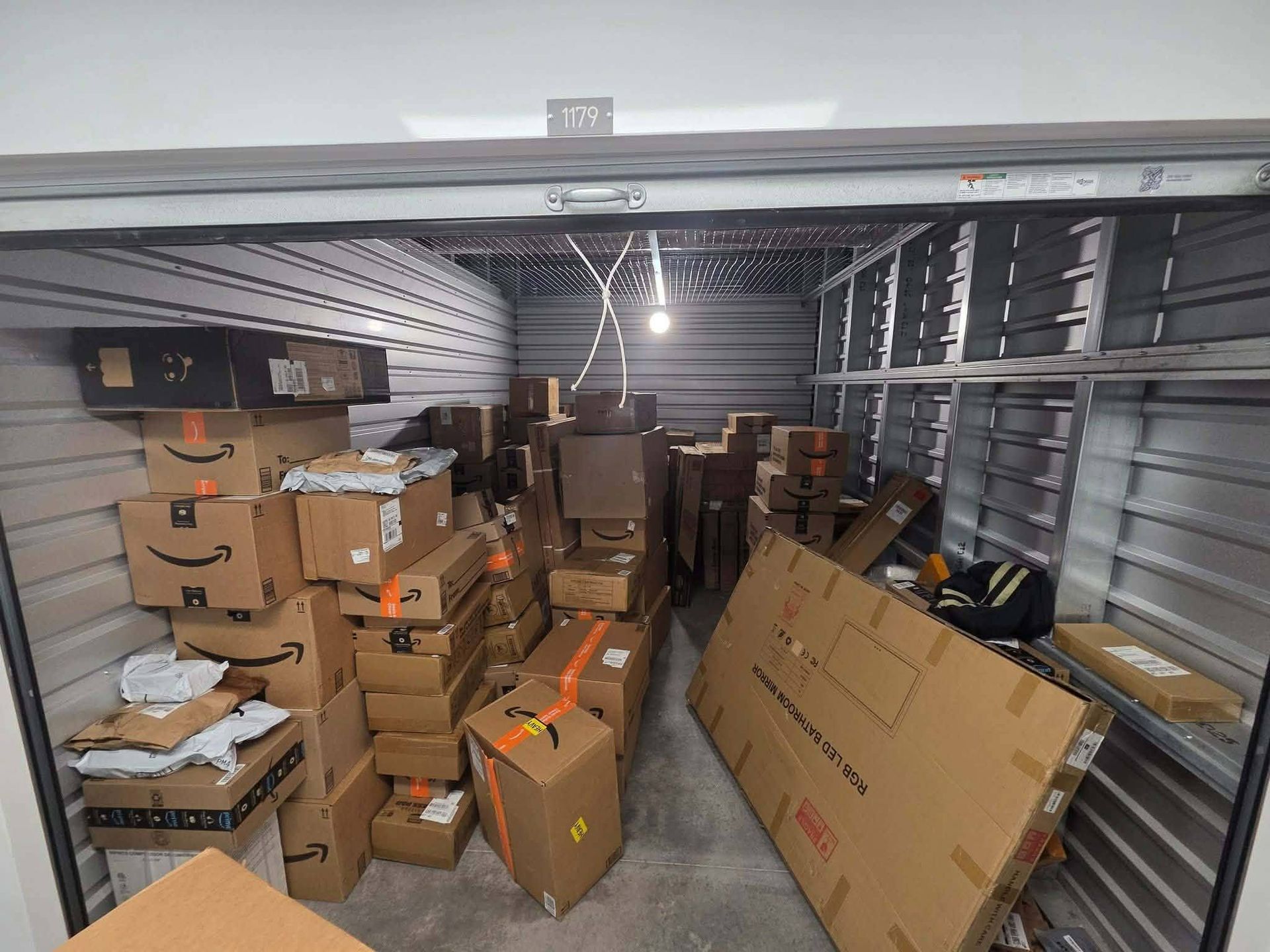 Packed storage unit filled with stacked cardboard boxes and loose items inside a metal-walled room