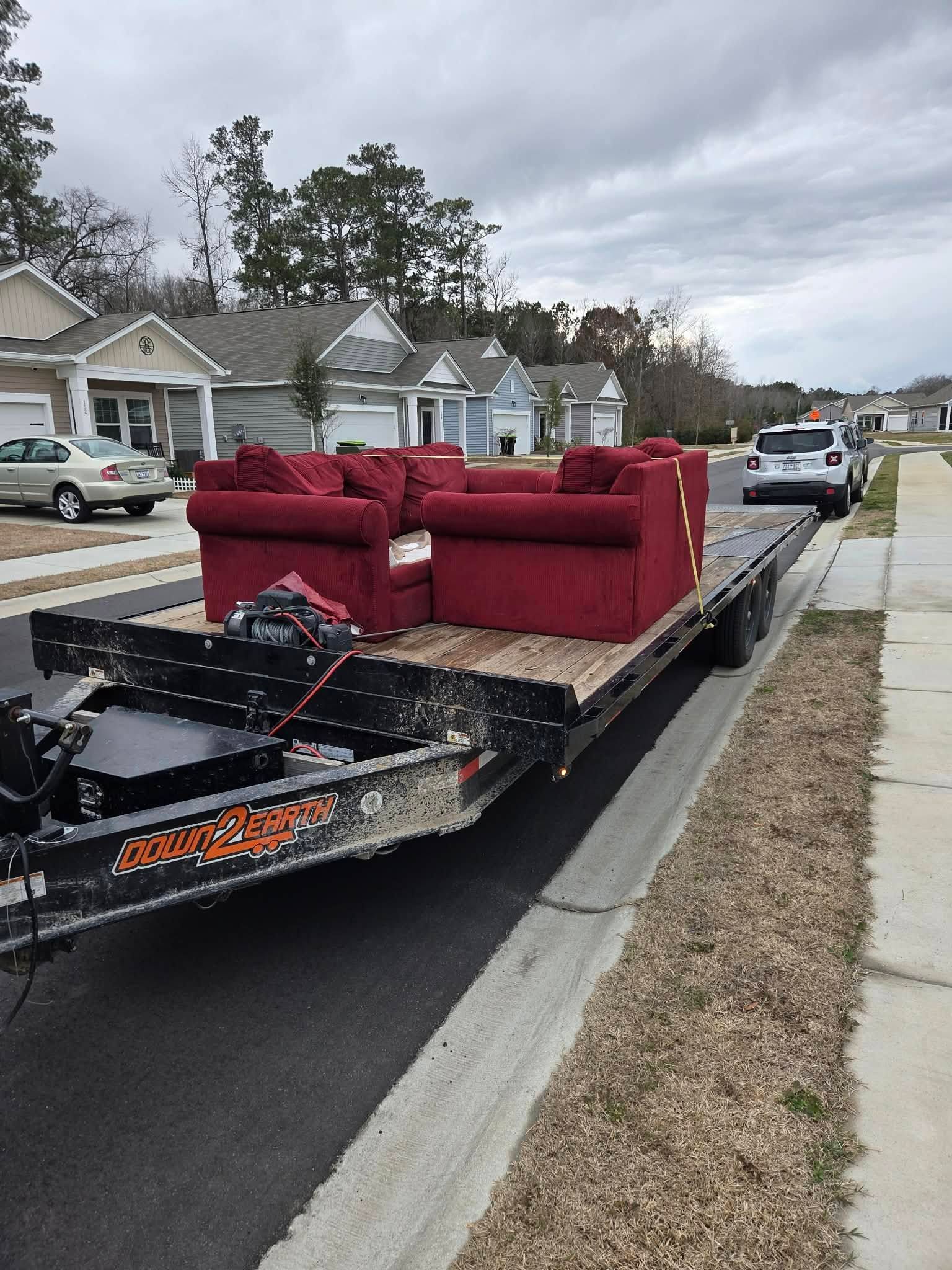 Red couch on a flatbed trailer parked on a residential street, with a damaged front end visible.