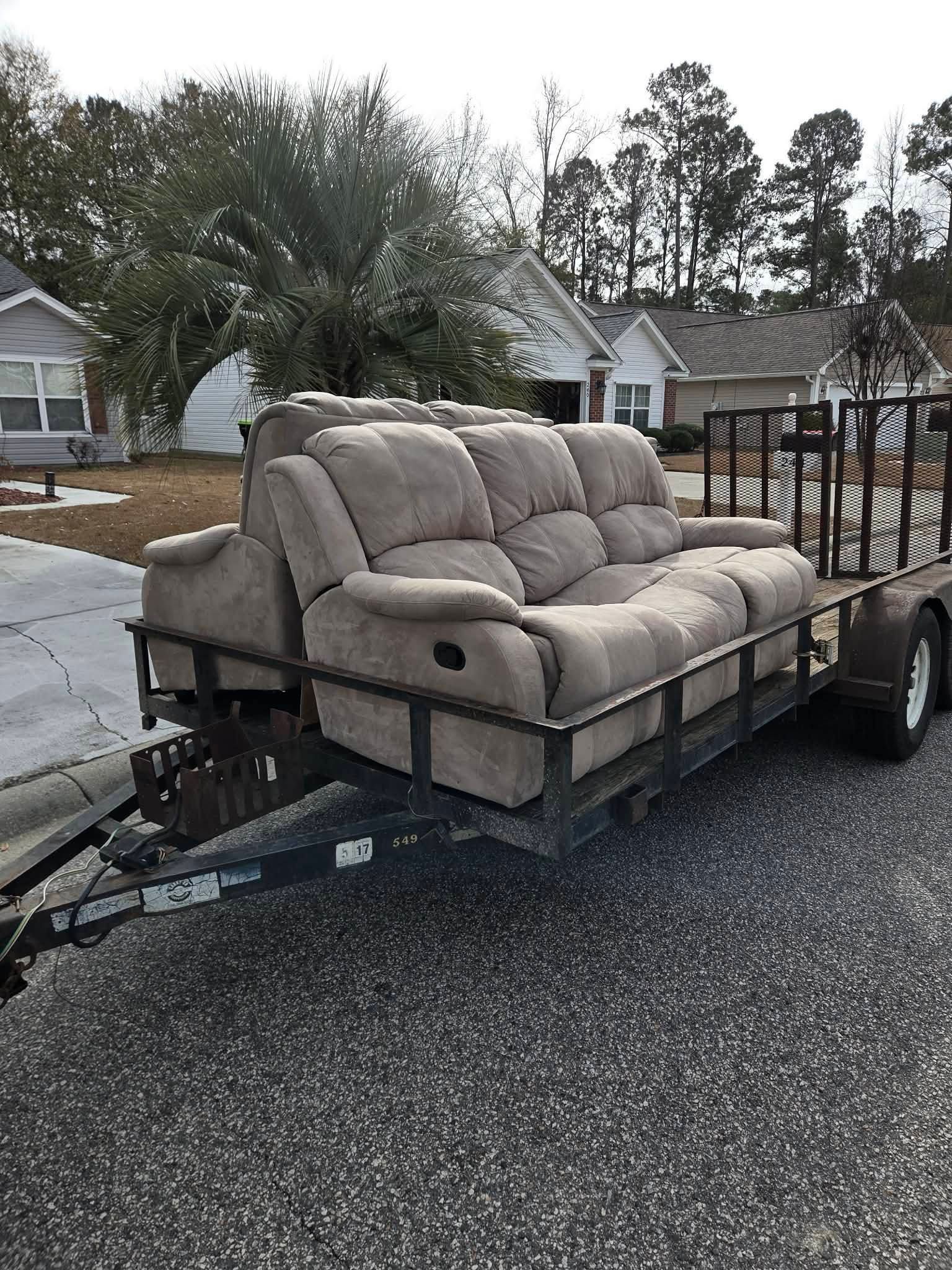 Beige sofa secured on a trailer parked by a residential street on a rainy day