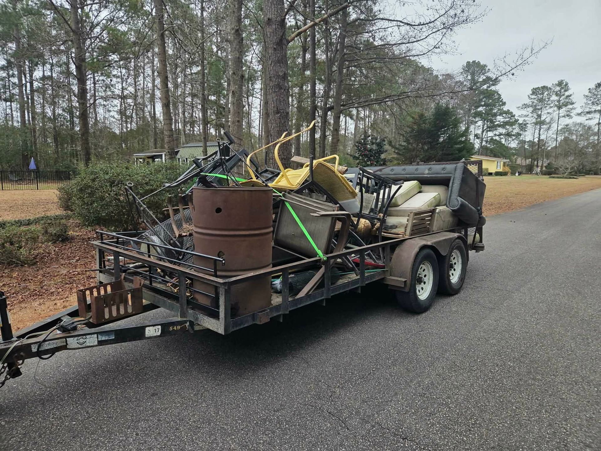 Trailer loaded with scrap metal and debris parked on a roadside near trees.