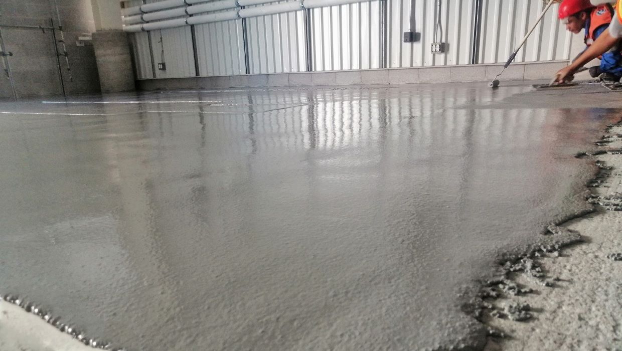 Un trabajador utiliza una herramienta para nivelar hormigón fresco y húmedo en un suelo industrial.