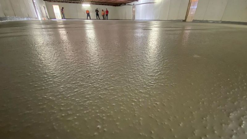 Vista desde un ángulo bajo de un suelo de hormigón texturizado recién vertido en una habitación con varias personas de pie al fondo.
