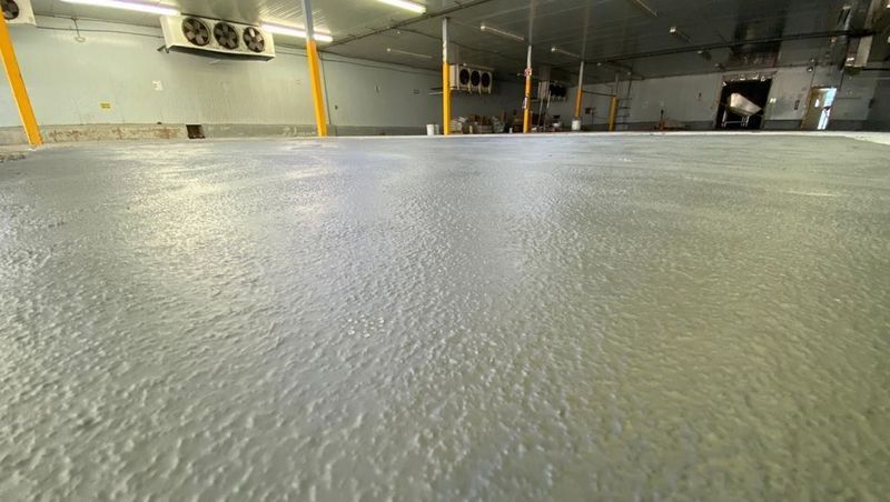 Vista desde un ángulo bajo de un suelo industrial gris y texturizado en el interior de un gran almacén frigorífico con unidades de refrigeración en el techo.