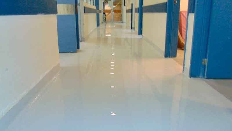 Un suelo blanco pulido y reflectante en un pasillo muy iluminado con paredes y puertas con detalles azules.
