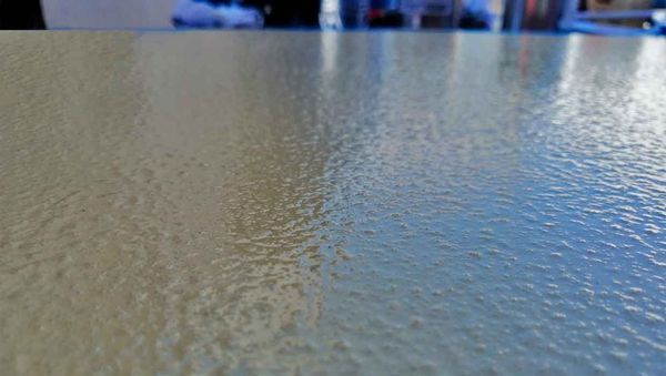 Primer plano y vista en ángulo de una superficie brillante de color beige con una ligera textura ondulada similar a la piel de naranja.