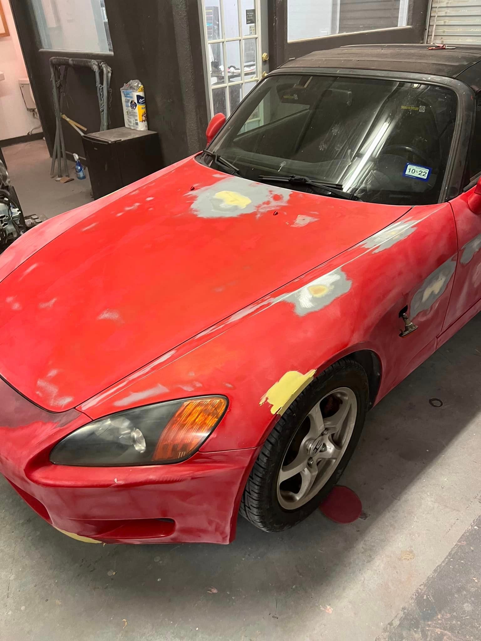 A red honda s2000 is being painted in a garage.