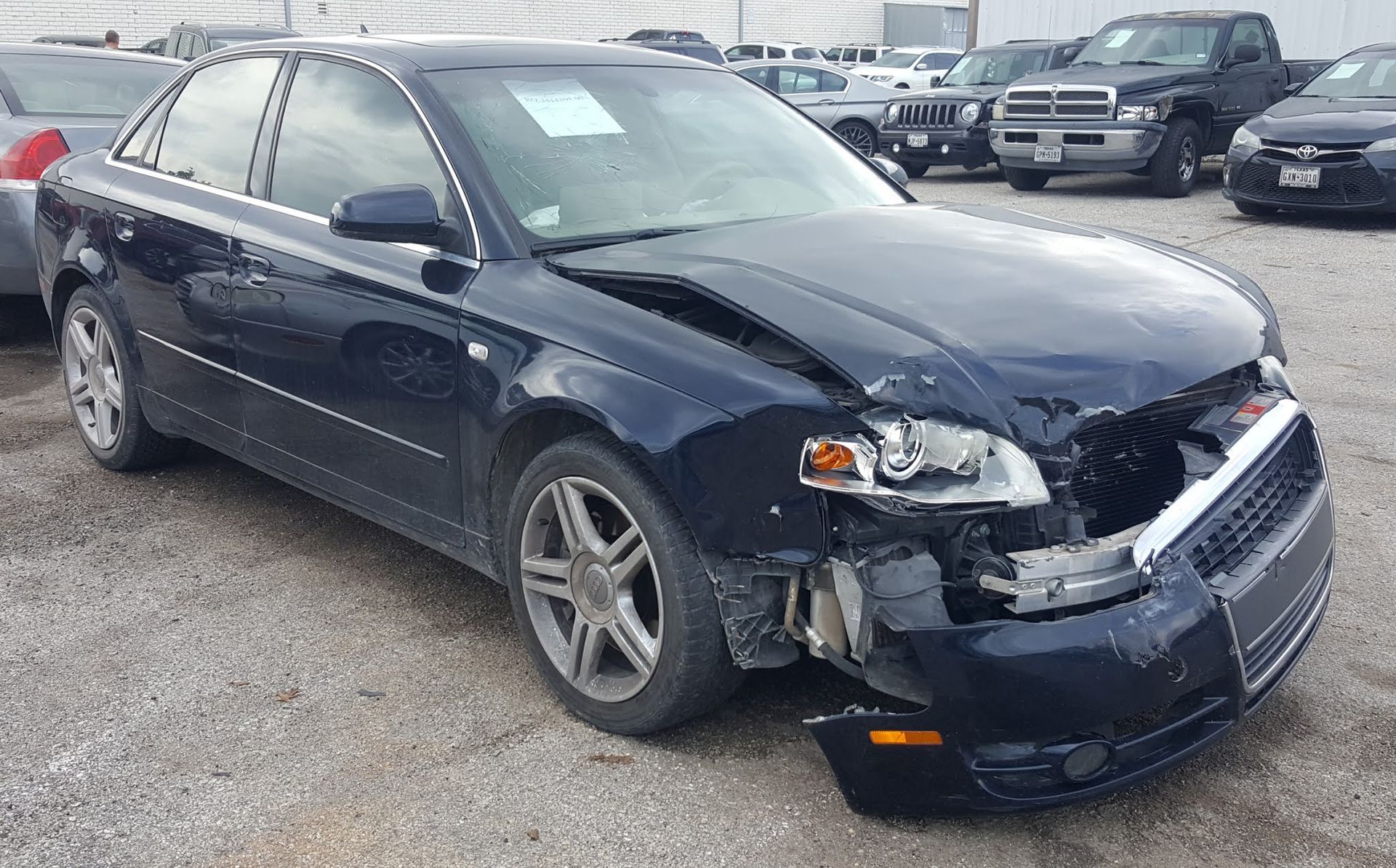 A blue car with a damaged front end is parked in a lot.