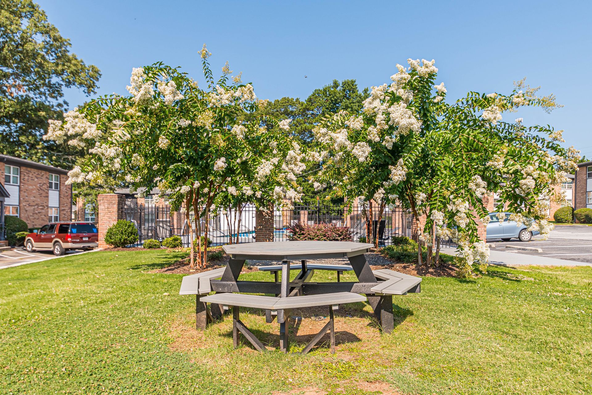 Brick courtyard with picnic tables under leafy trees beside apartment buildings