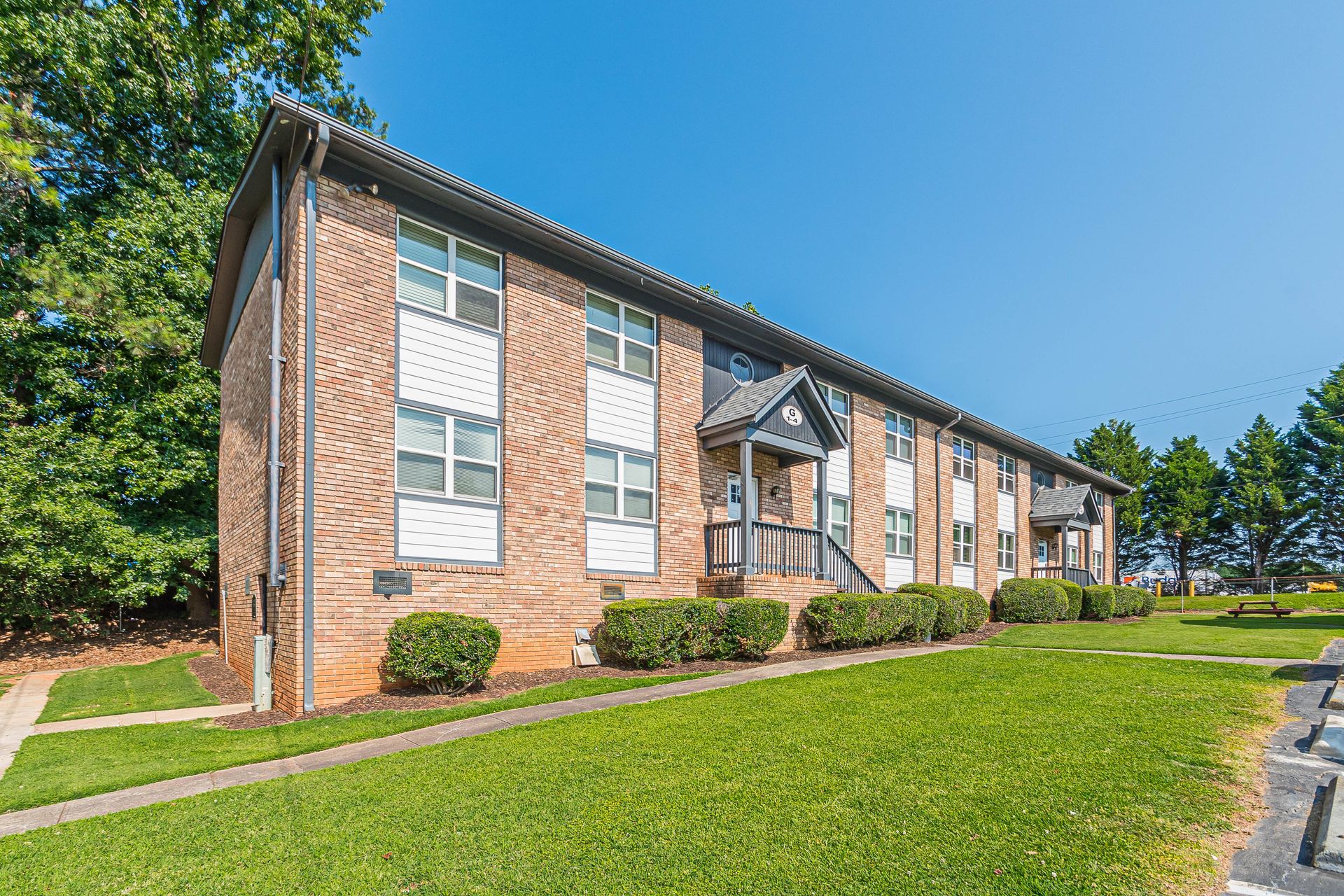 Brick apartment building with white-trimmed windows and green lawn on a sunny day