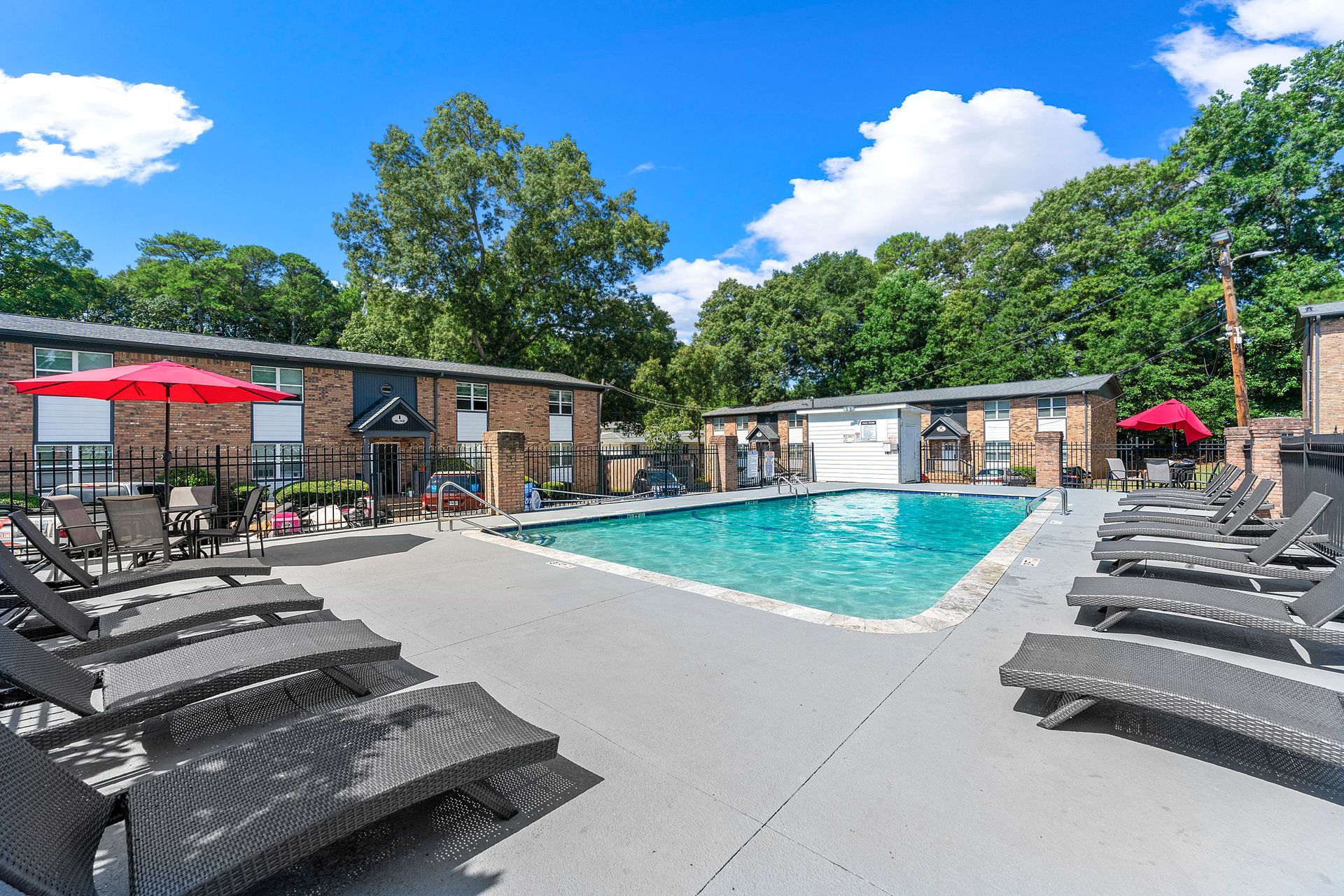 Apartment pool courtyard with lounge chairs, umbrellas, and a bright blue sky