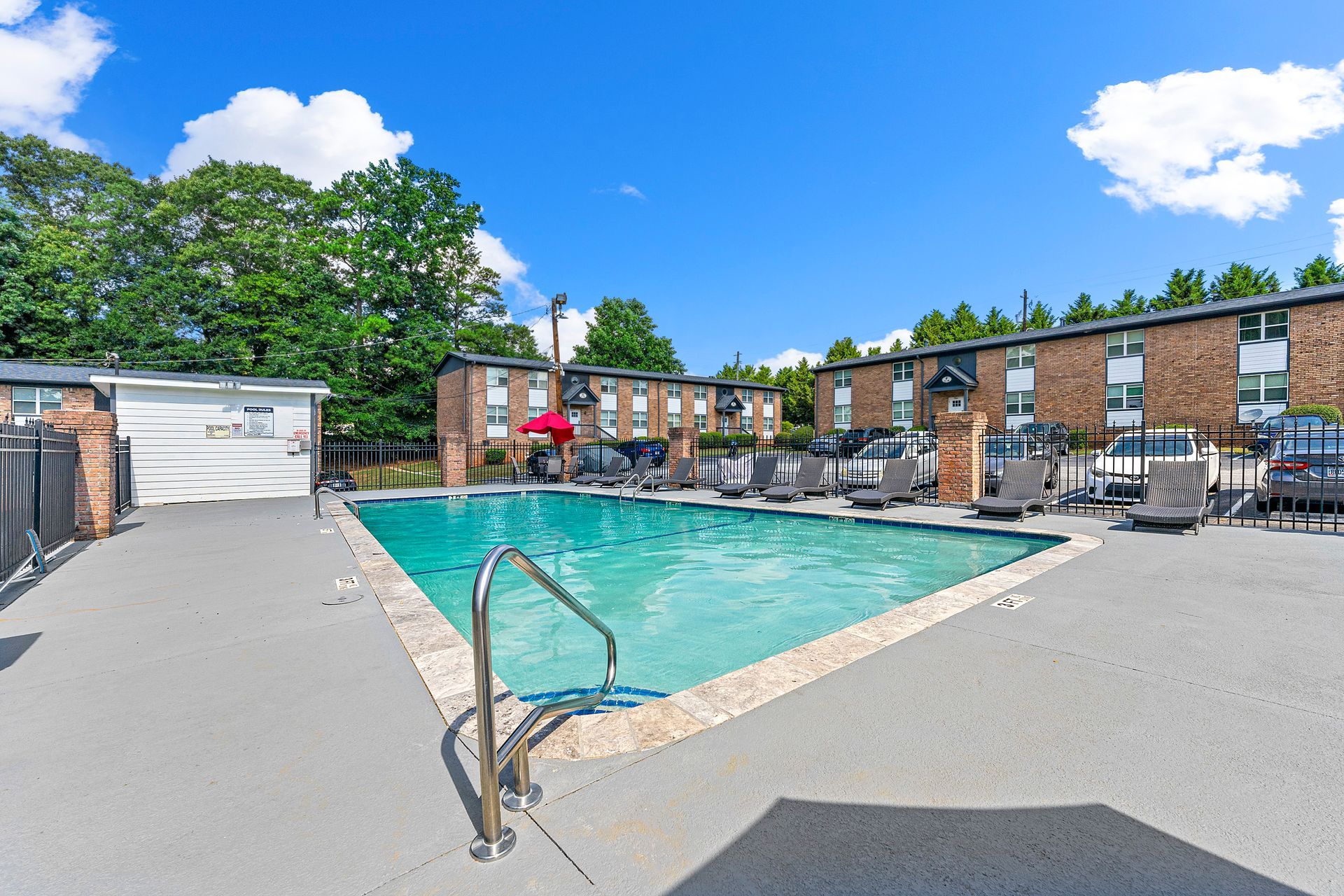 Outdoor swimming pool with lounge chairs and a brick apartment courtyard under a blue sky