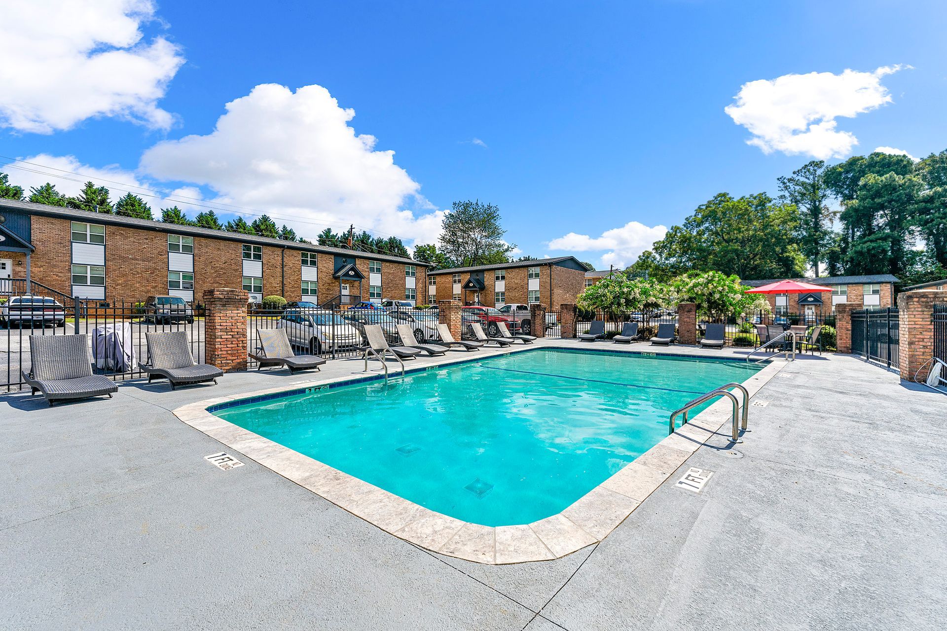 Outdoor apartment pool with turquoise water and lounge chairs under a blue sky