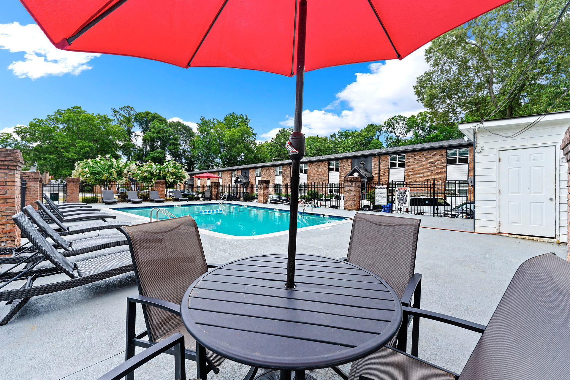 Poolside patio with red umbrella, table, lounge chairs, and apartment buildings in the background
