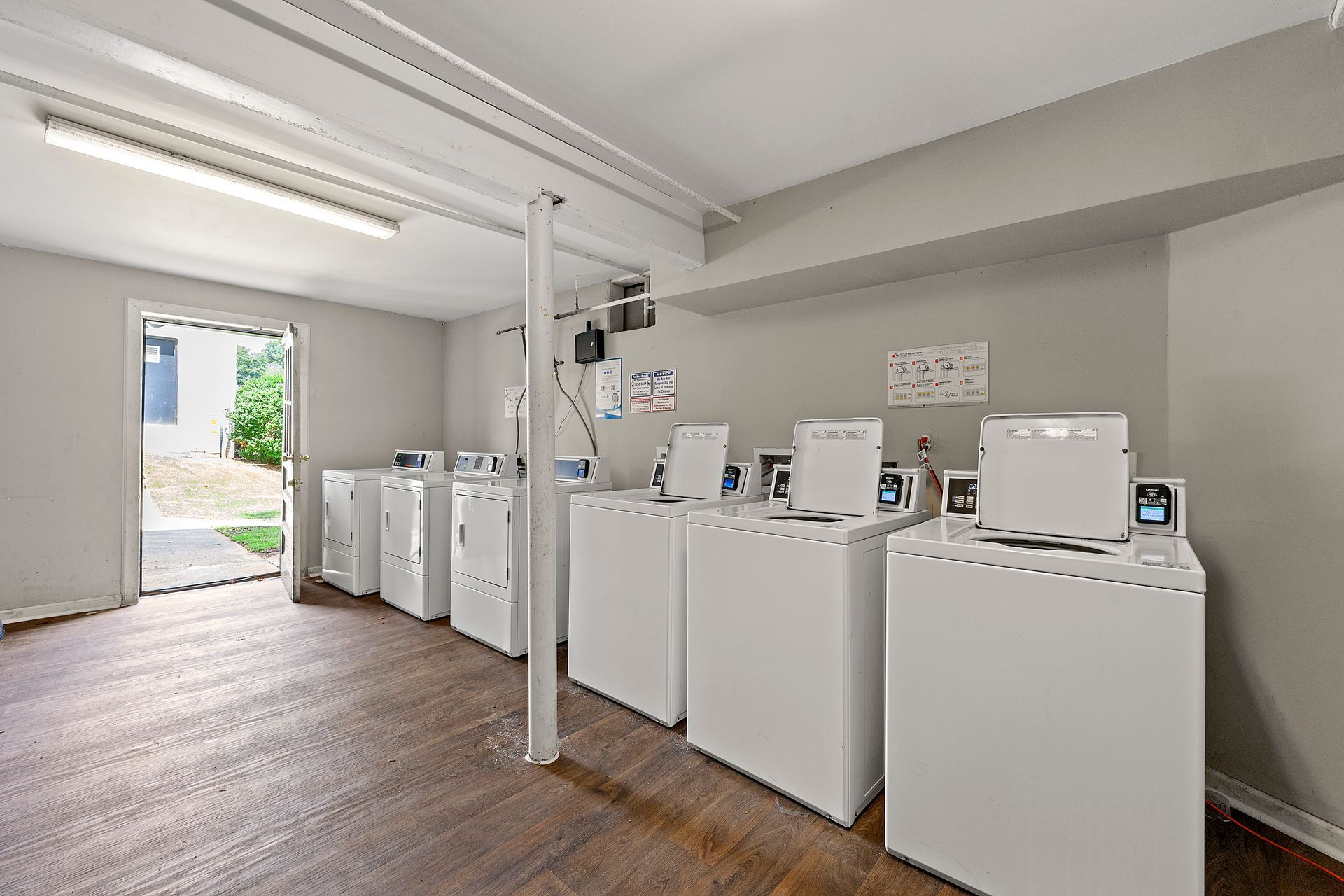 Bright laundromat interior with rows of white washing machines and dryers on a wood floor