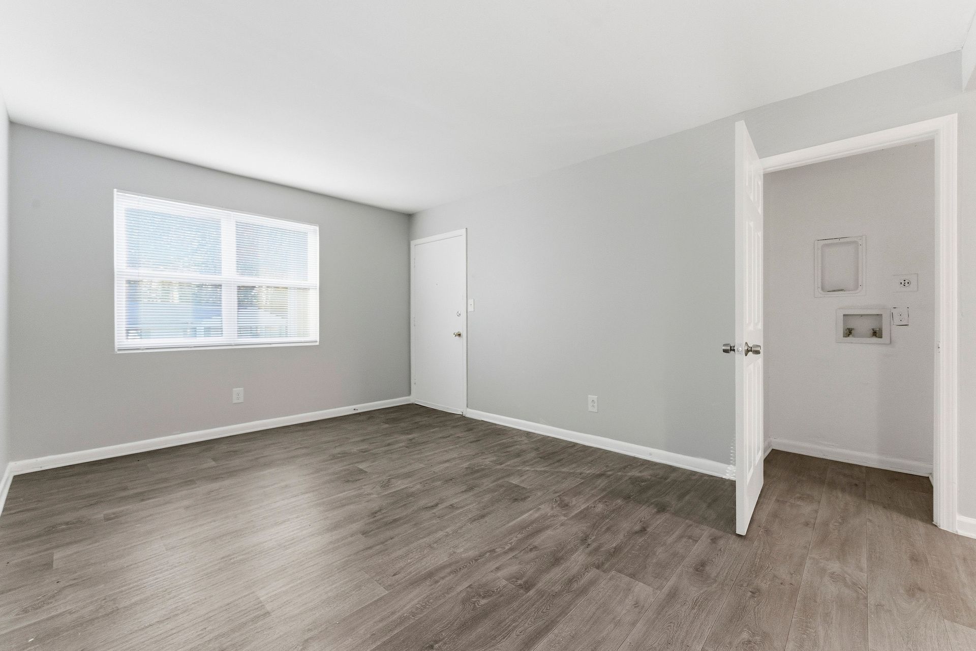Empty gray bedroom with white trim, wood-look floor, window blinds, and an open door to a closet area