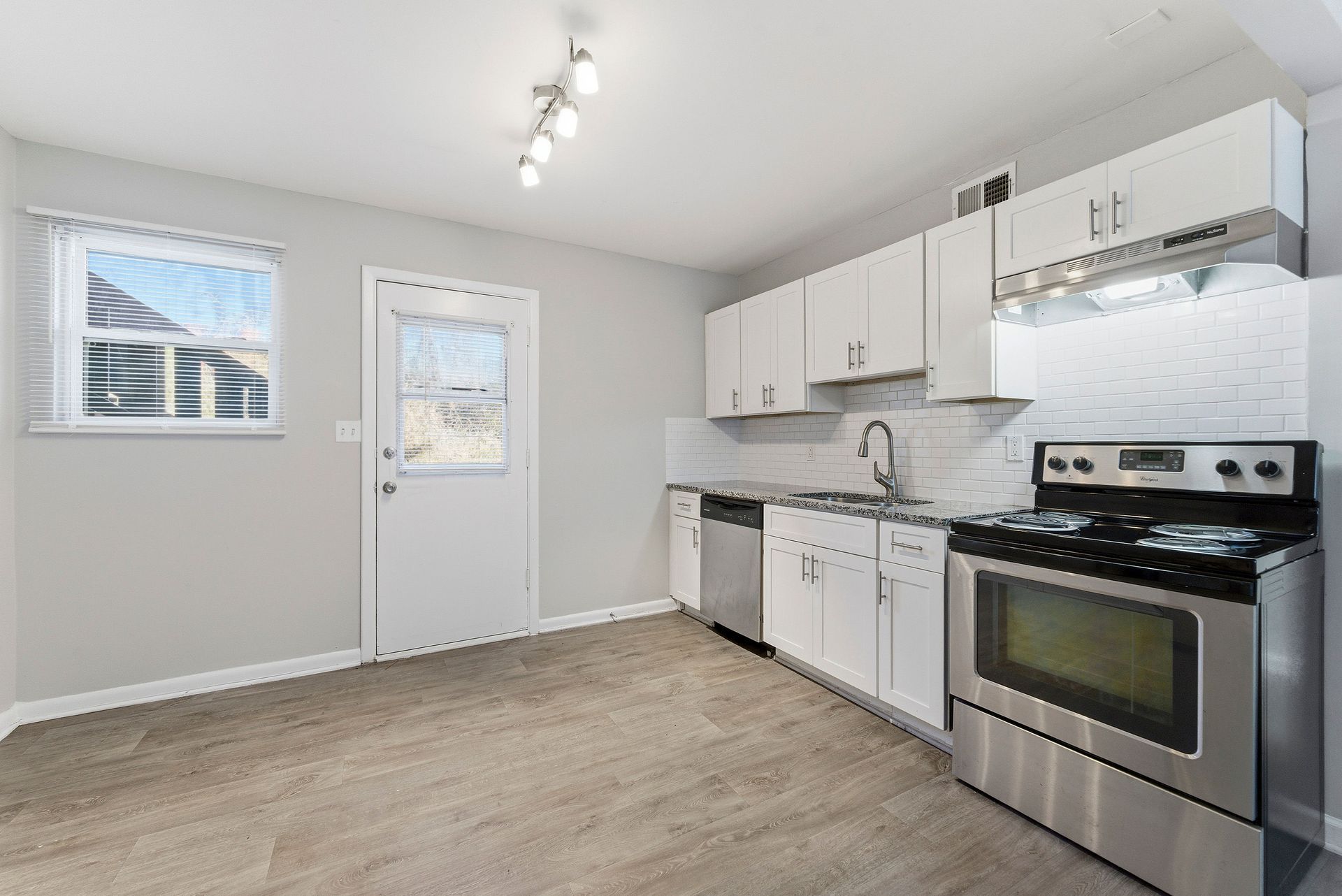 Empty white kitchen with stainless steel stove, white cabinets, and gray flooring