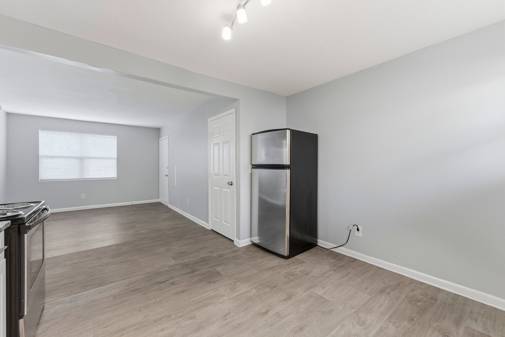 Empty gray kitchen and living area with a stainless steel refrigerator and wood-look flooring