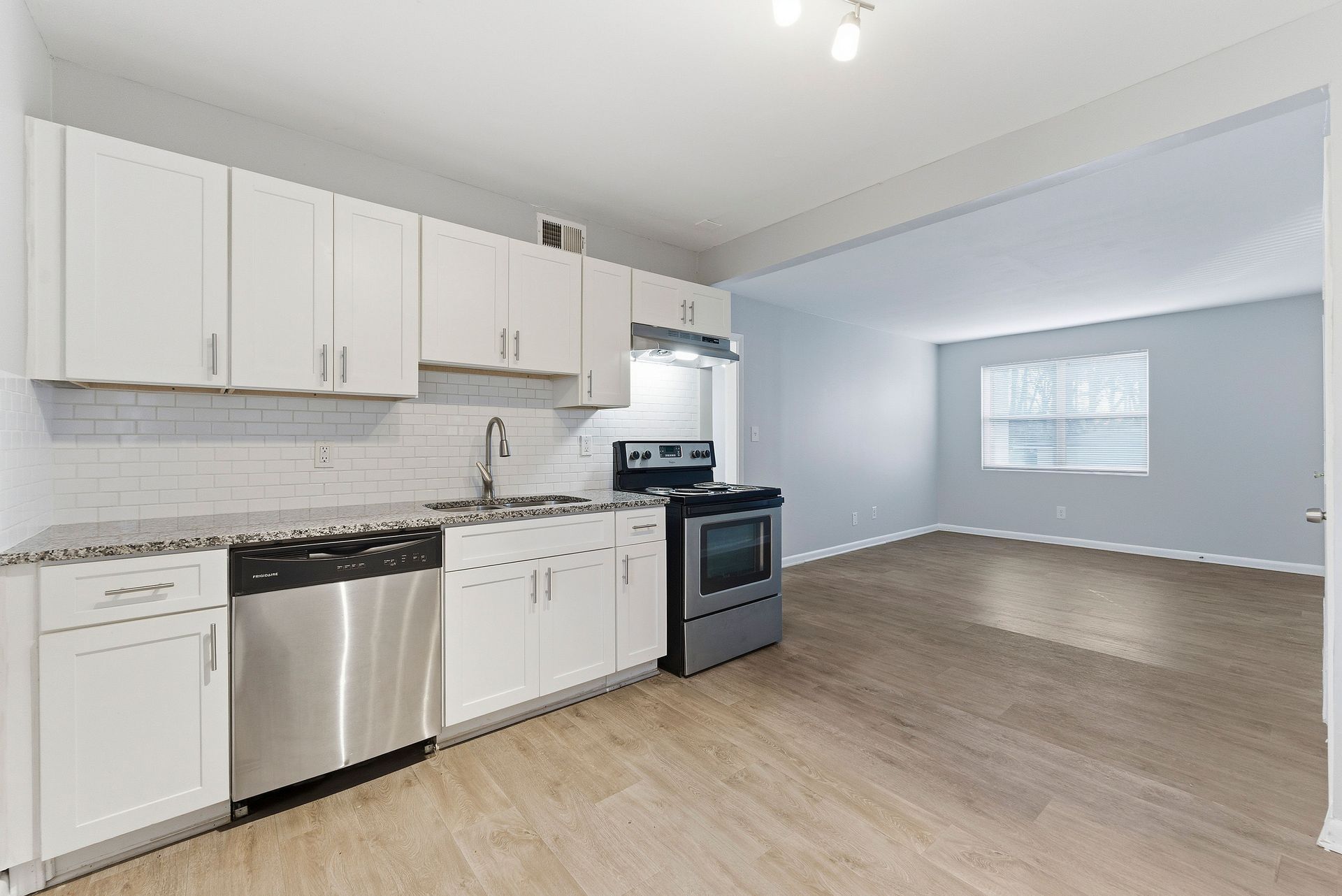 Bright kitchen with white cabinets, stainless steel appliances, and open light-blue living area with wood floors