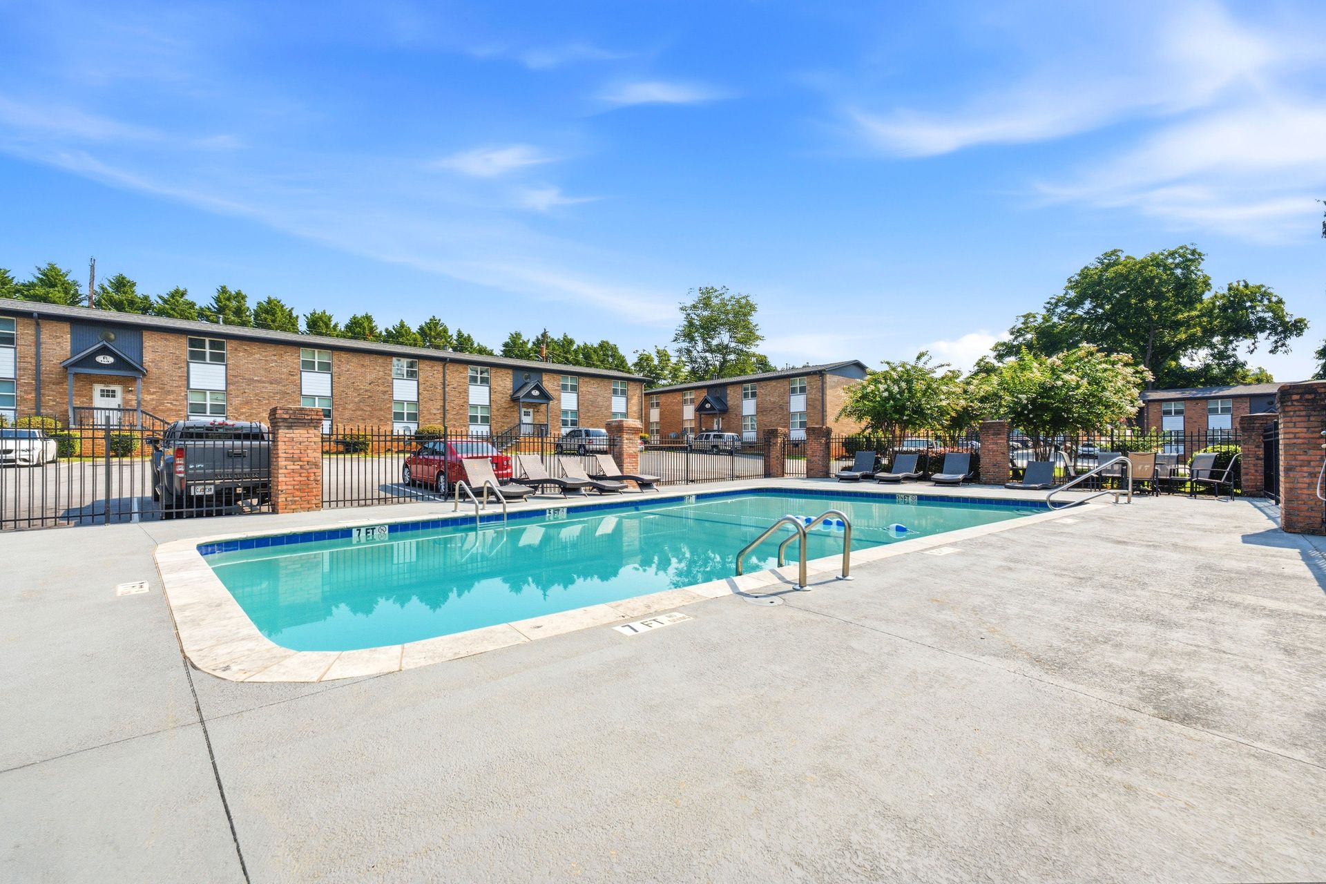 Outdoor apartment complex swimming pool with turquoise water and brick buildings under a blue sky