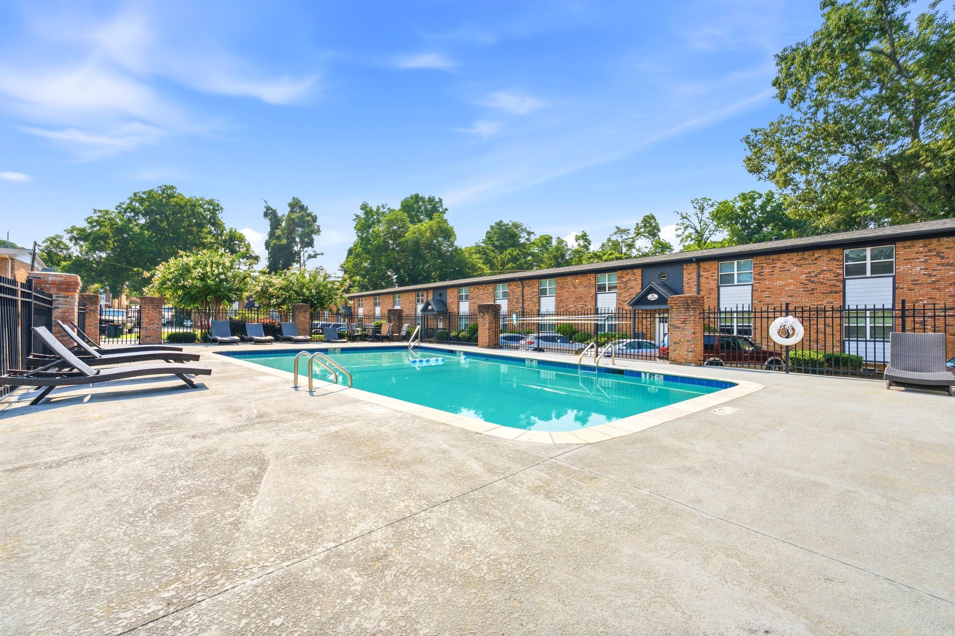 Outdoor apartment pool with blue water, lounge chairs, and brick buildings under a clear sky