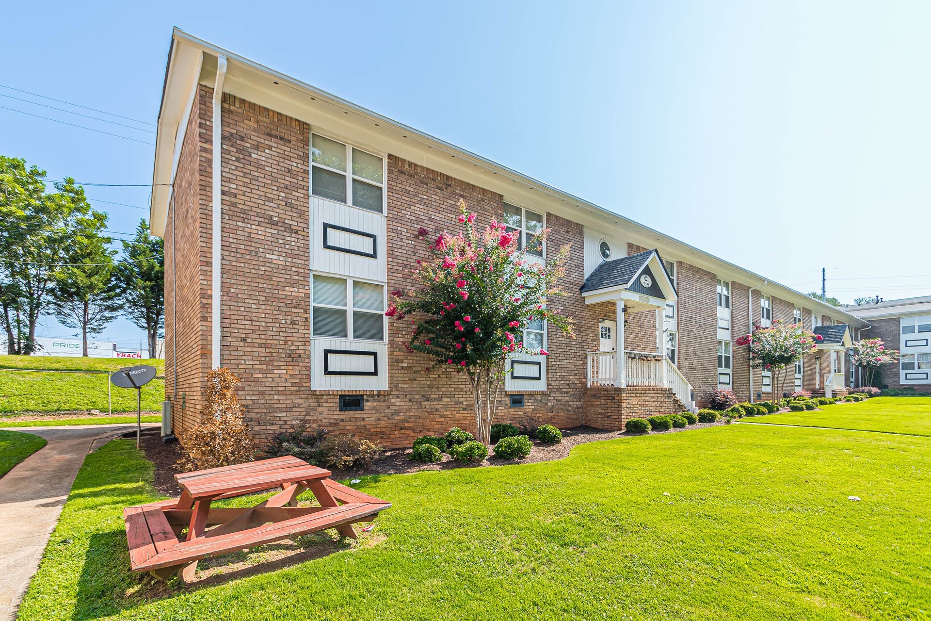 Brick apartment building with white trim, grassy lawn, and a picnic table under a bright blue sky