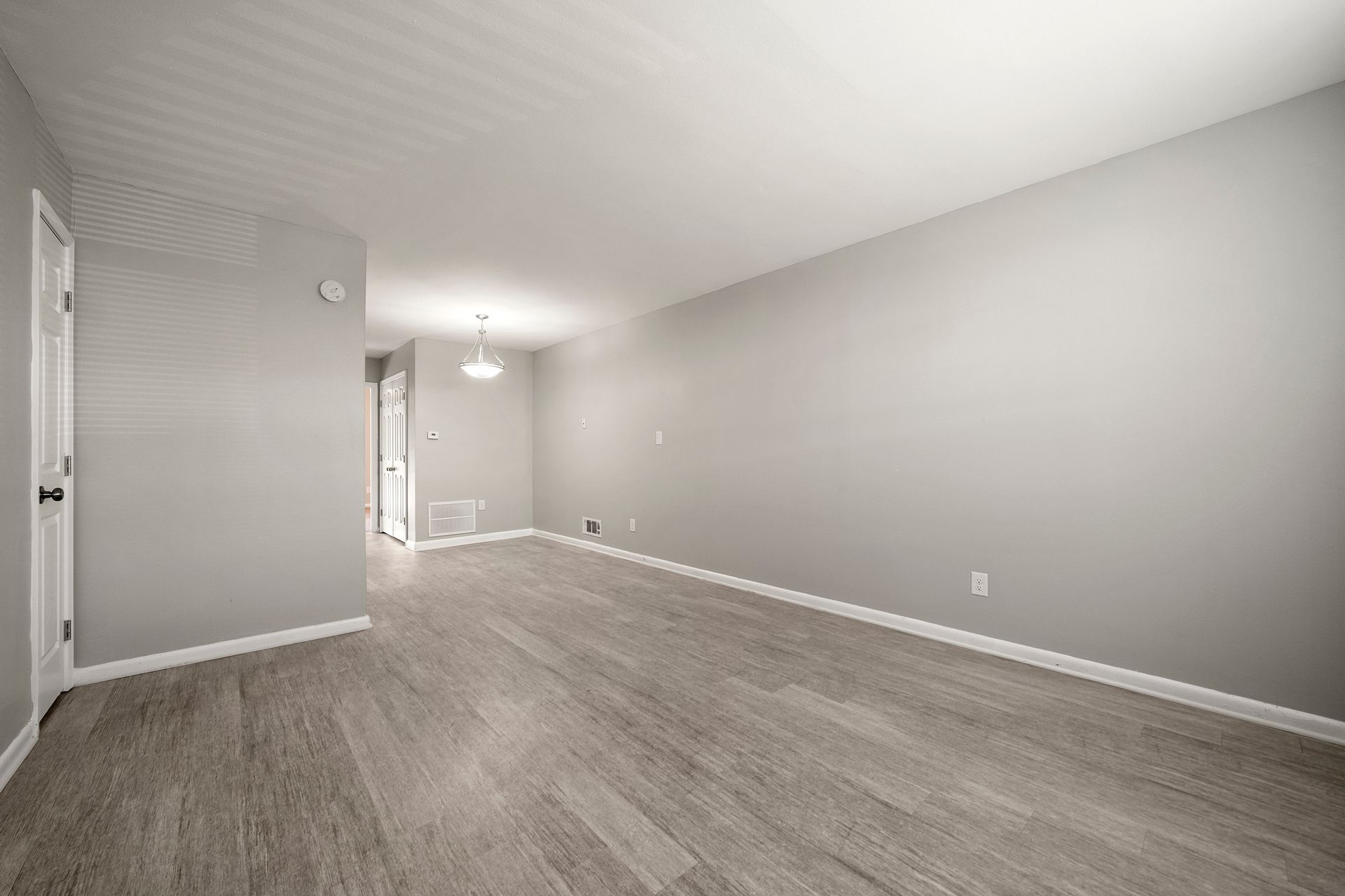 Empty gray living room with wood-look flooring, white trim, and recessed lighting.