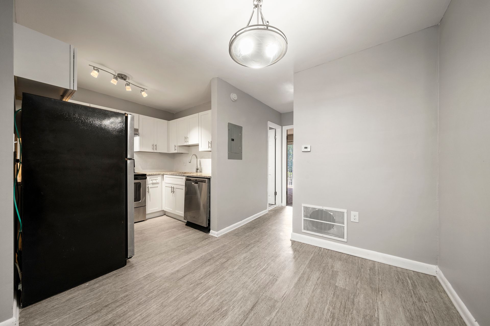 Empty modern apartment kitchen and dining area with black refrigerator and gray wood floors
