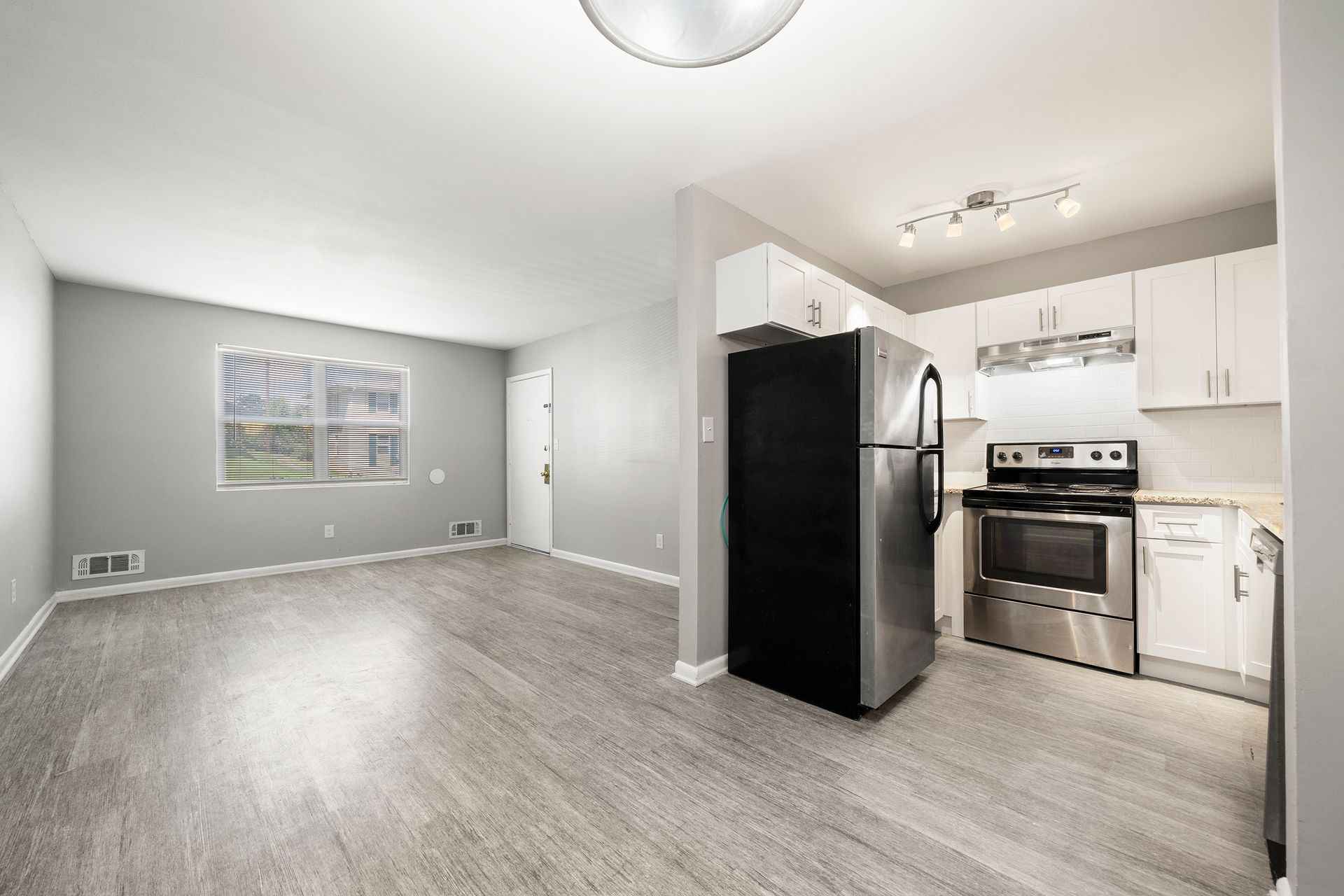 Empty modern kitchen and living area with gray floors, white cabinets, and black appliances