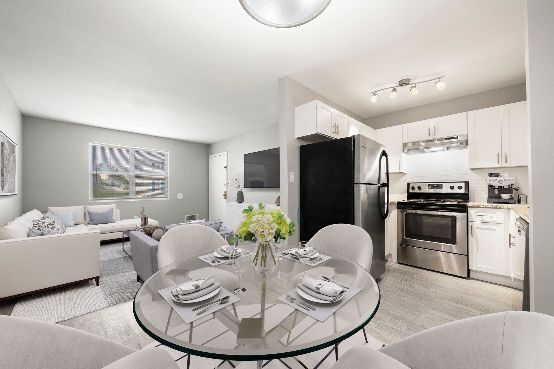 Bright open-plan living room and kitchen with glass dining table, white sofa, and black refrigerator