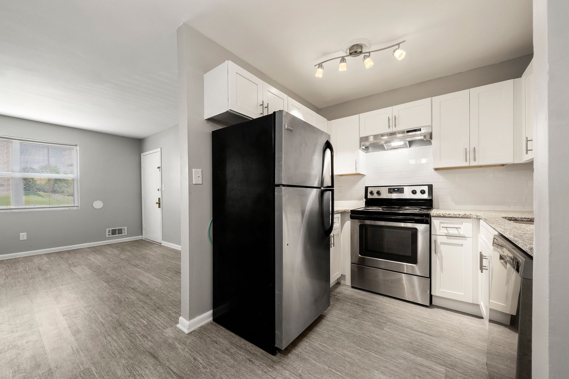Open kitchen with white cabinets, stainless steel appliances, and black refrigerator beside a gray living area