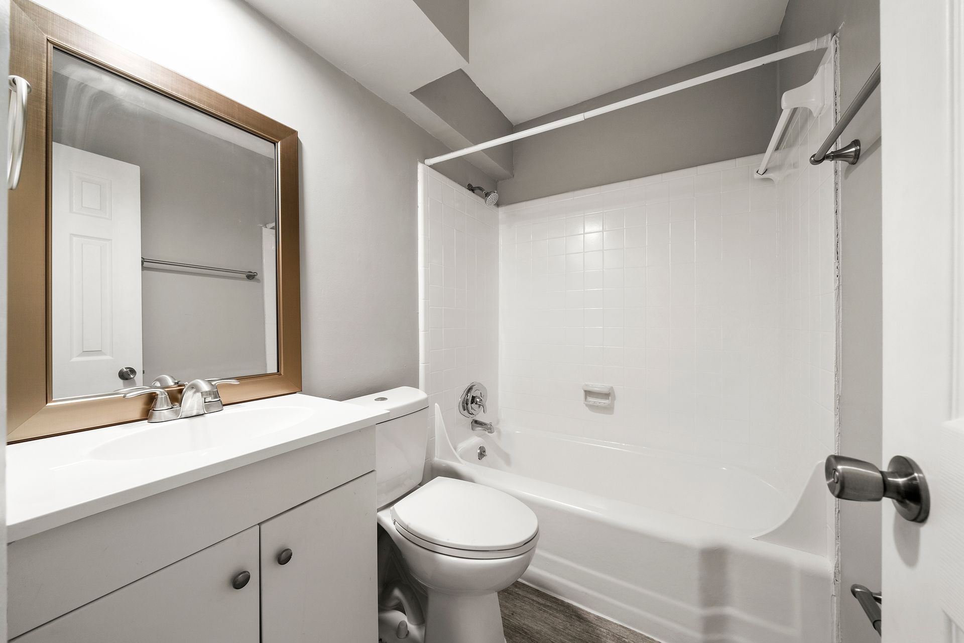Small white bathroom with vanity, mirror, toilet, and bathtub with shower curtain rod