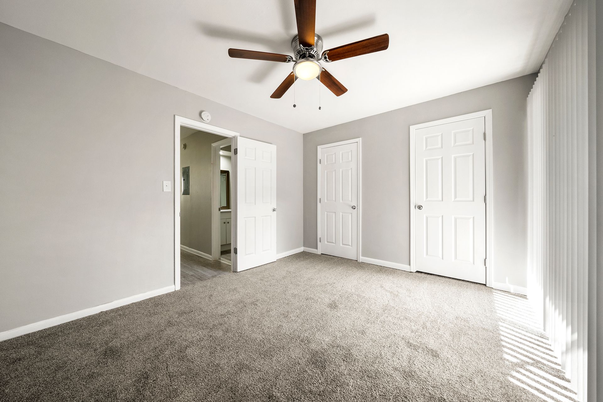 Empty gray-carpeted bedroom with white doors, light walls, and a ceiling fan