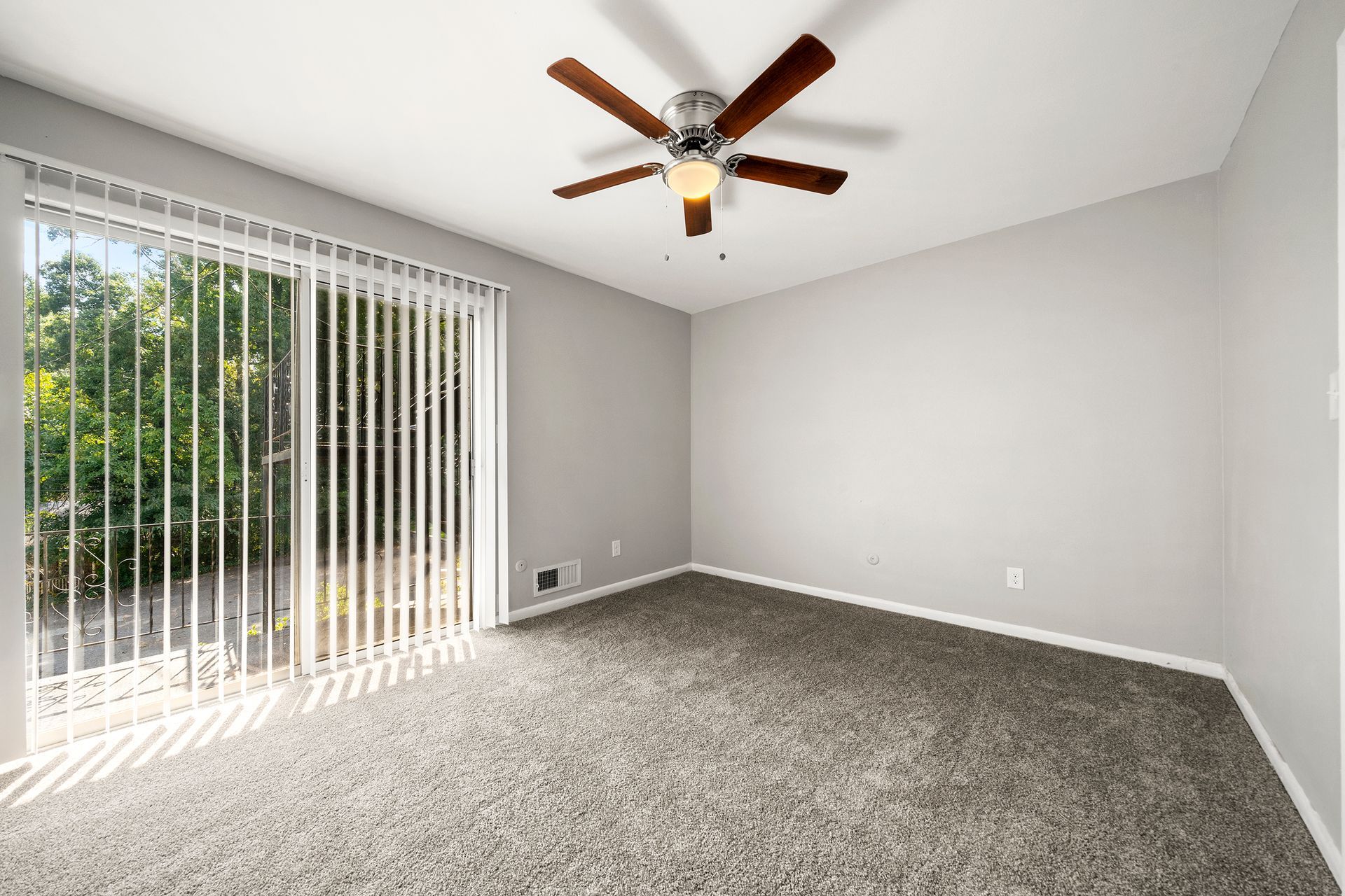 Empty carpeted room with ceiling fan, gray walls, and sliding glass door with vertical blinds