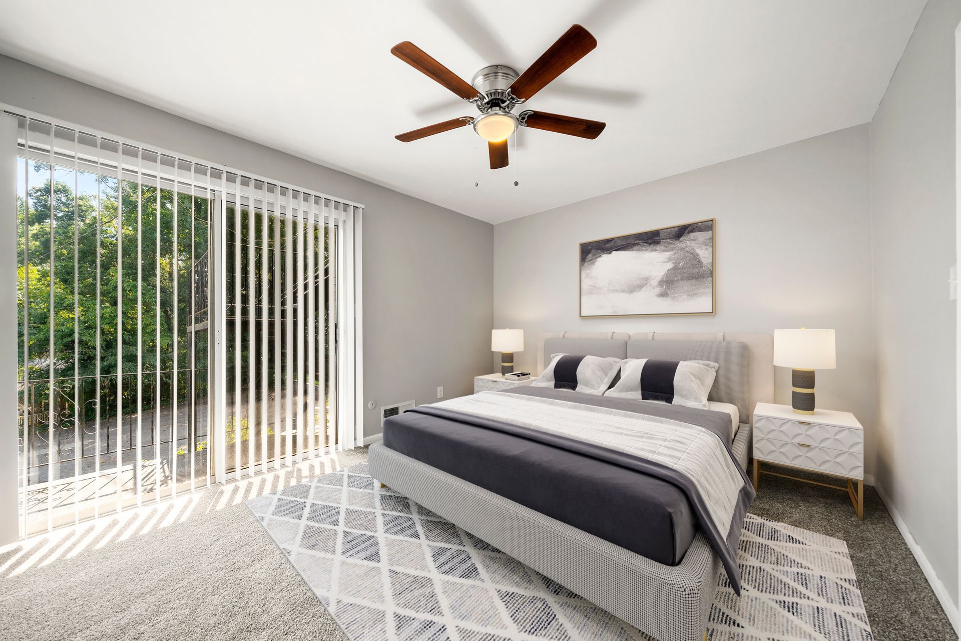 Bright bedroom with king bed, gray decor, nightstand, ceiling fan, and sliding glass door to greenery