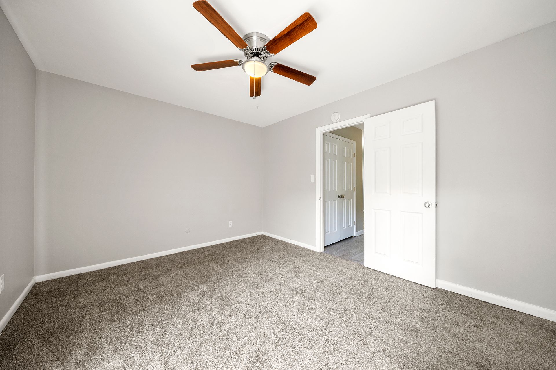 Empty bedroom with gray walls, carpeted floor, and a ceiling fan near an open door