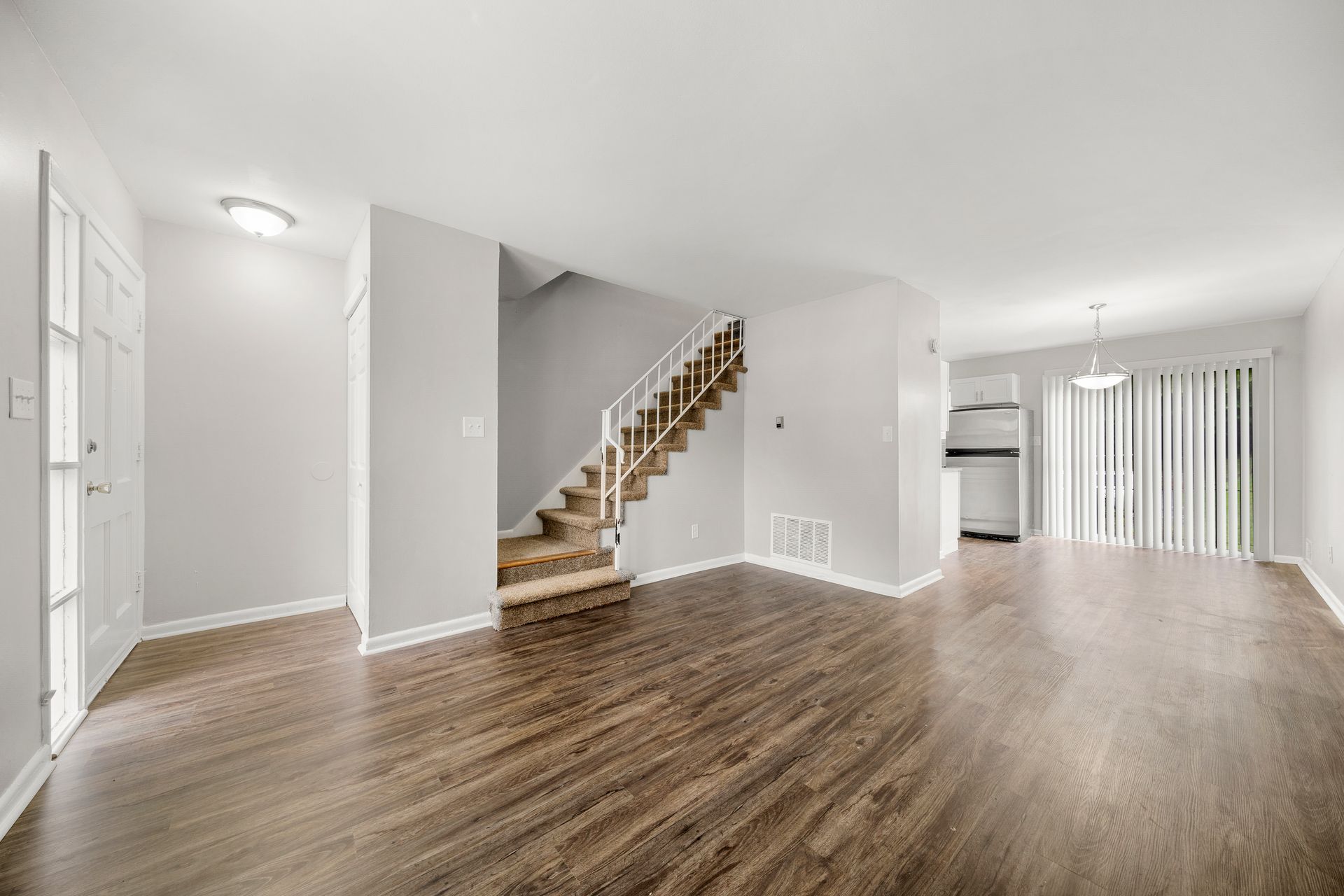 Empty modern living room with wood floors, staircase, and sliding glass doors