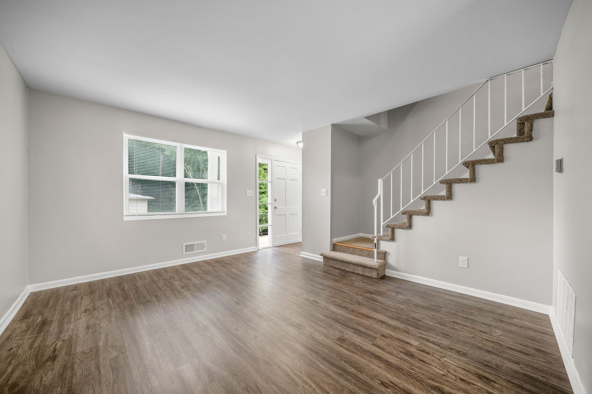 Empty living room with gray walls, wood floors, and a staircase along the right wall.