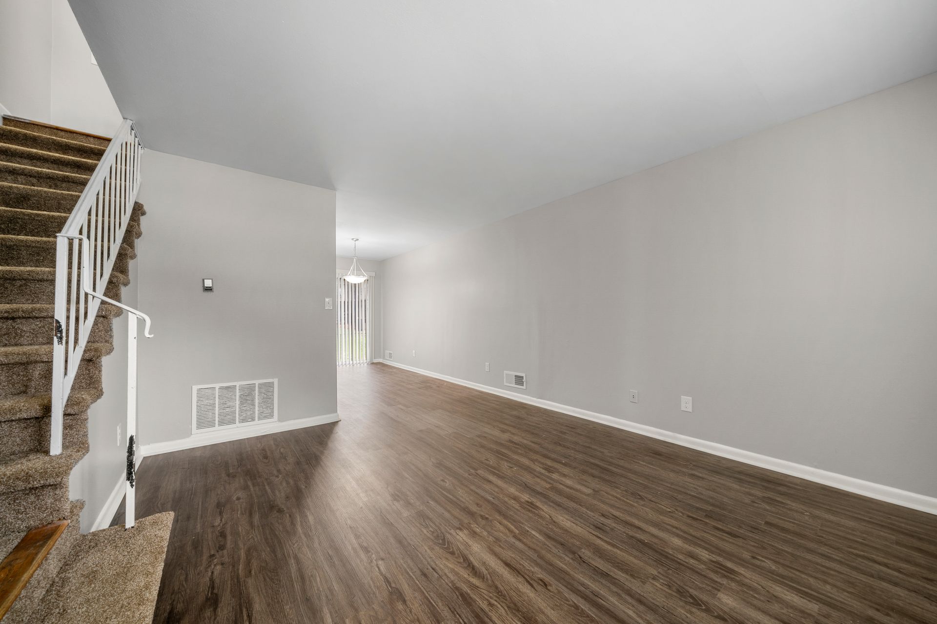 Empty living room with gray walls, brown wood floors, and staircase on the left