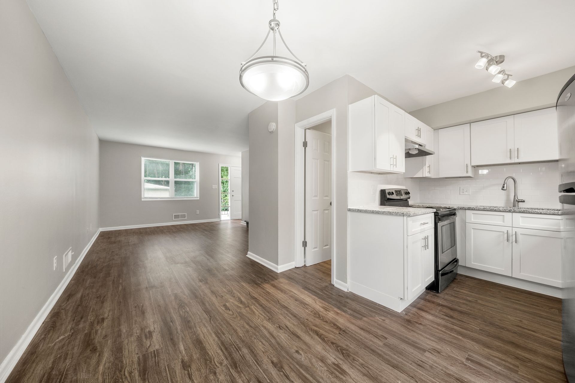 Empty open-plan living room and white kitchen with wood-look flooring and pendant lights