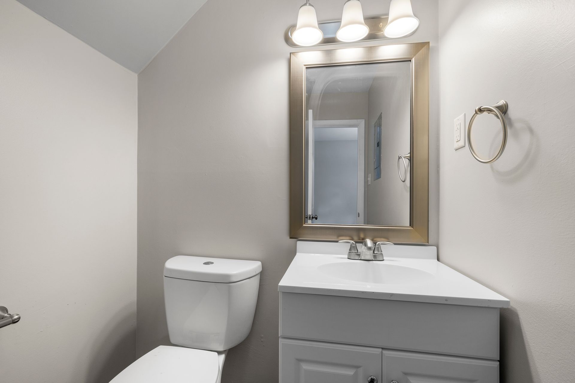 Small bathroom with white toilet, gray vanity, mirror, and three-light fixture.