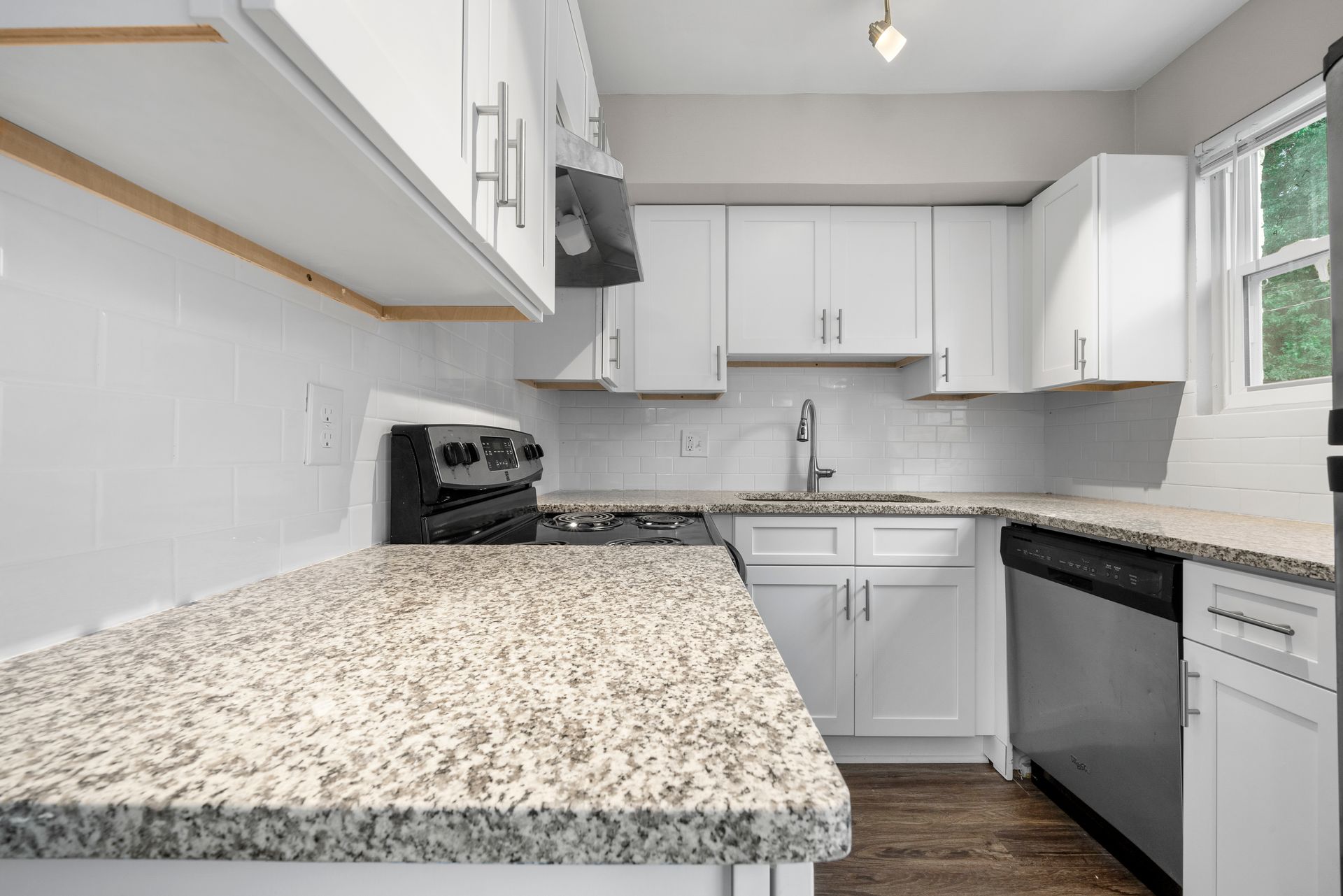 Bright white kitchen with granite counters, black appliances, and a window above the sink