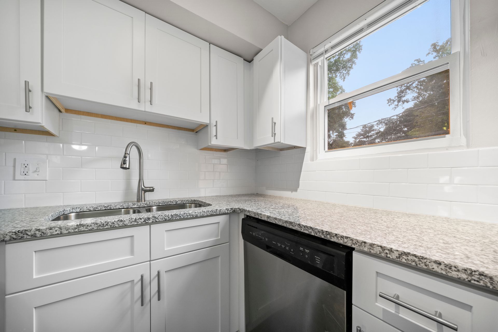 Bright white kitchen with granite counters, stainless sink, dishwasher, and a window above the counter.