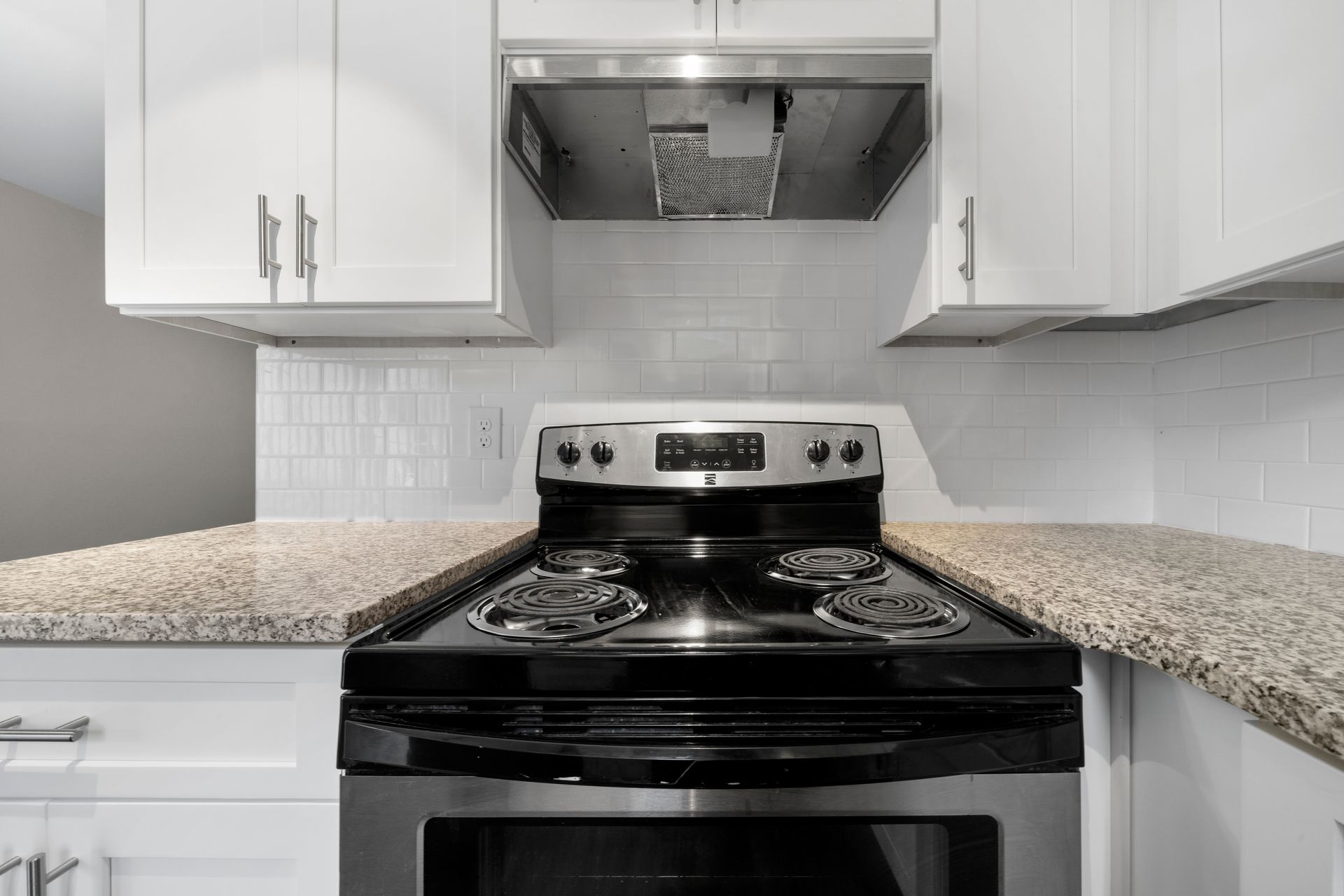 Modern white kitchen with black stove, granite counters, and stainless steel range hood