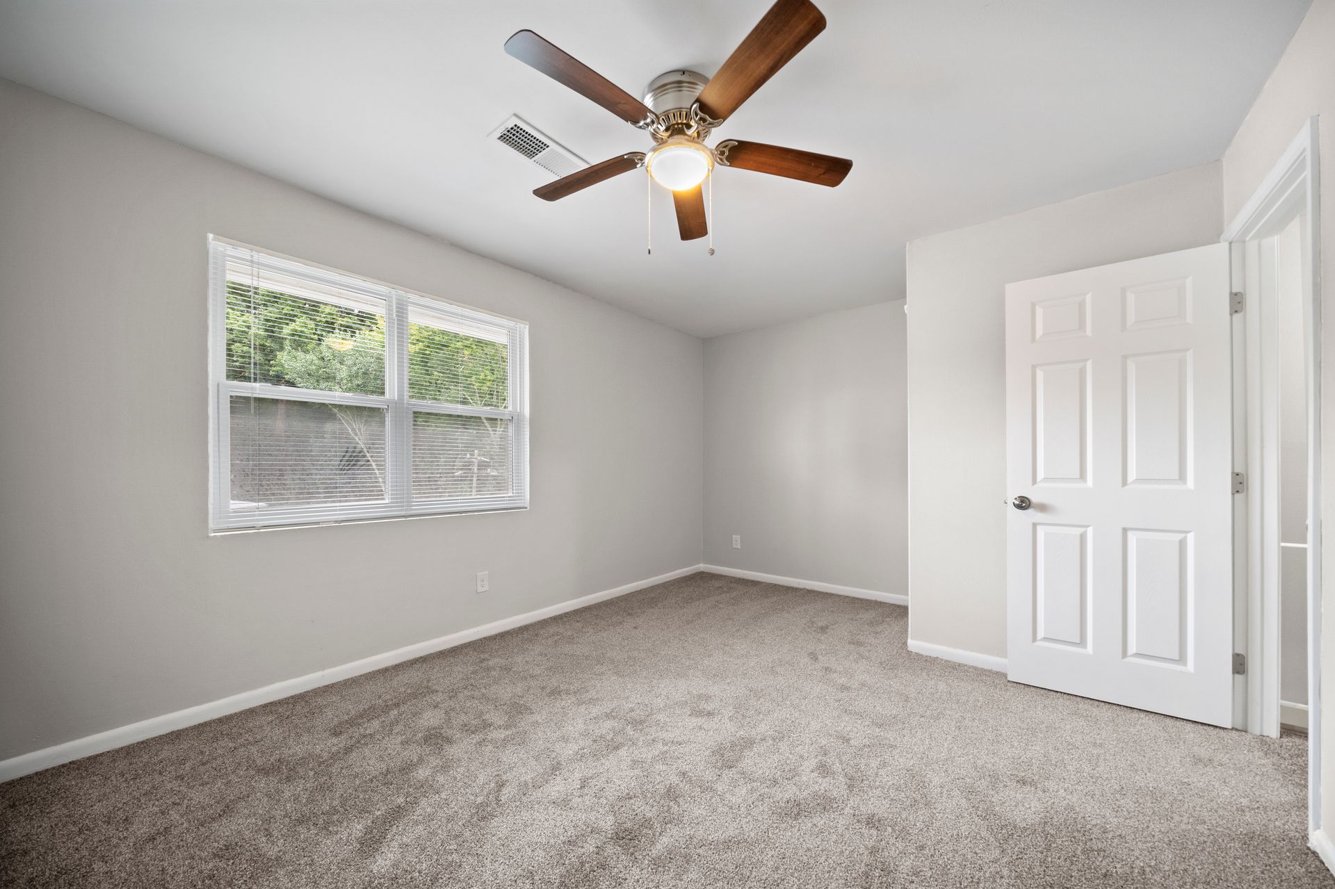 Empty carpeted bedroom with white walls, window blinds, and a ceiling fan.