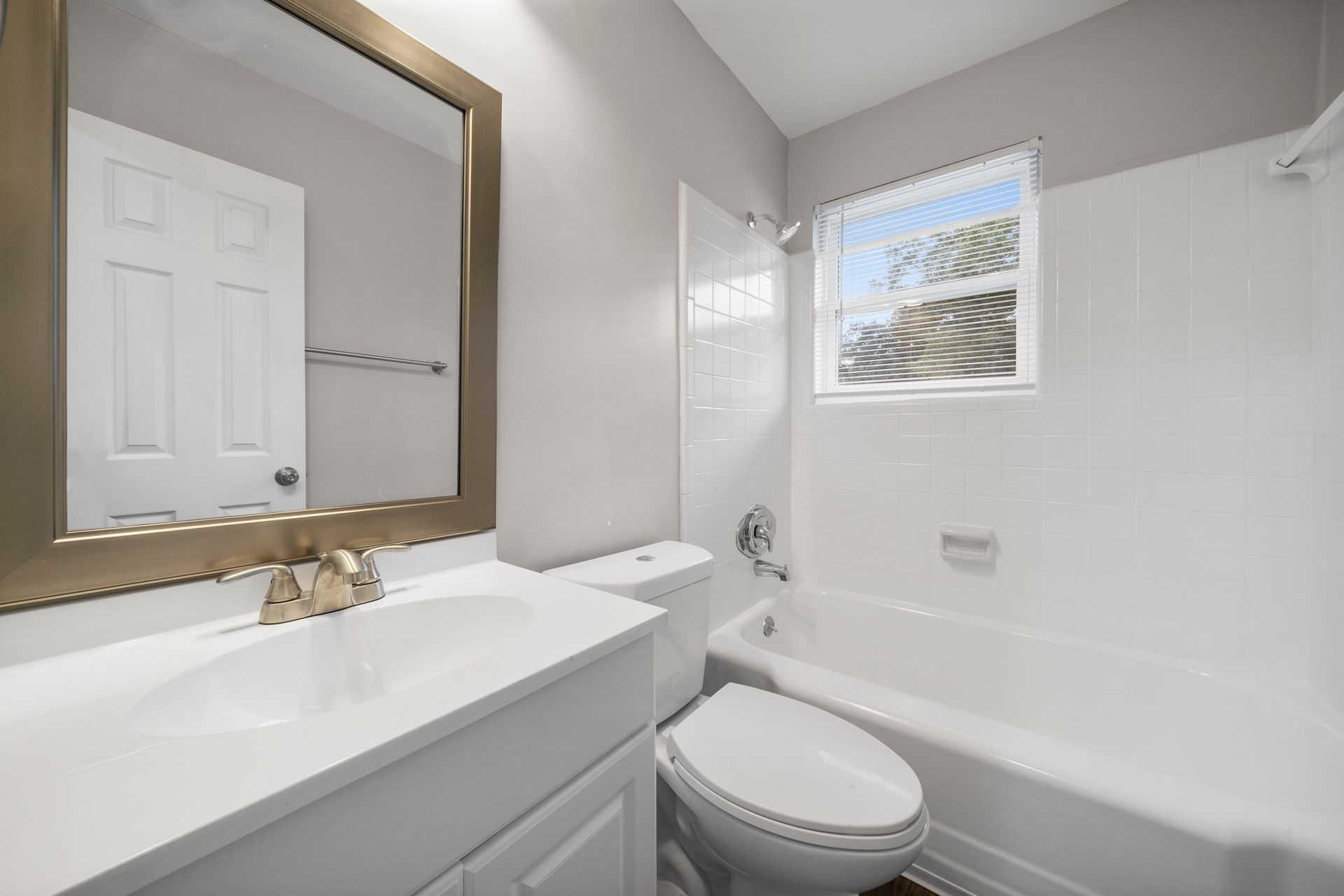 Bright white bathroom with vanity, mirror, toilet, and bathtub beneath a small window