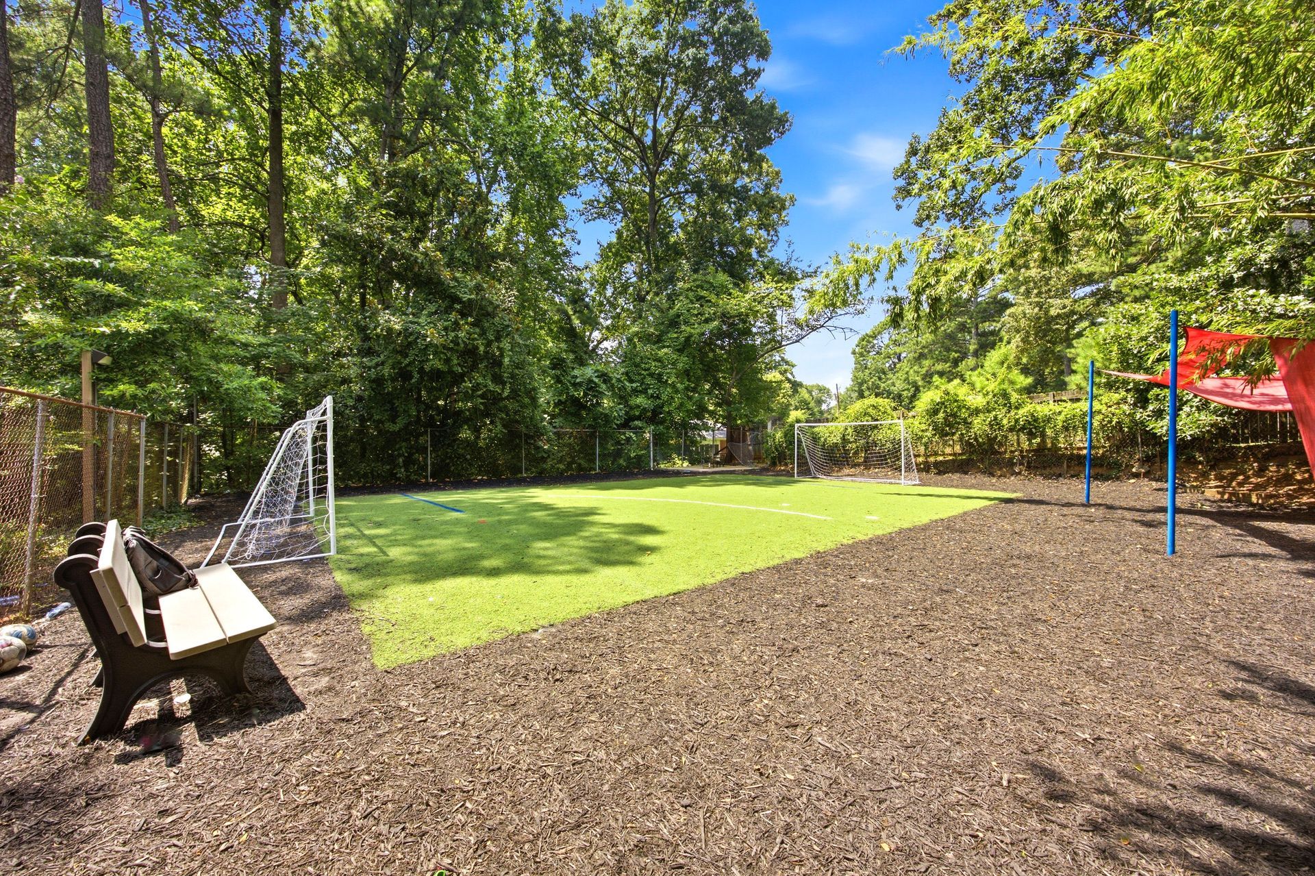Sunny playground with wood chips, bench, swing, and trees under a clear blue sky