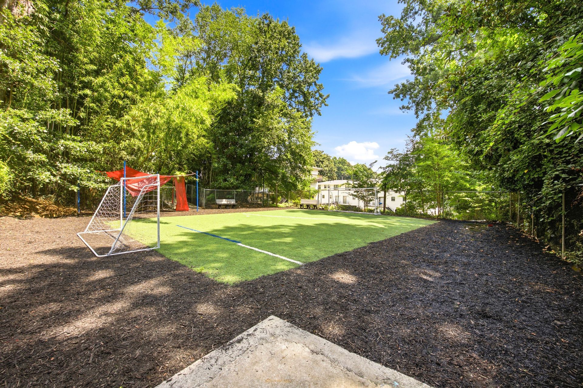 Backyard playground with a small red play set, green grass, and trees under a blue sky