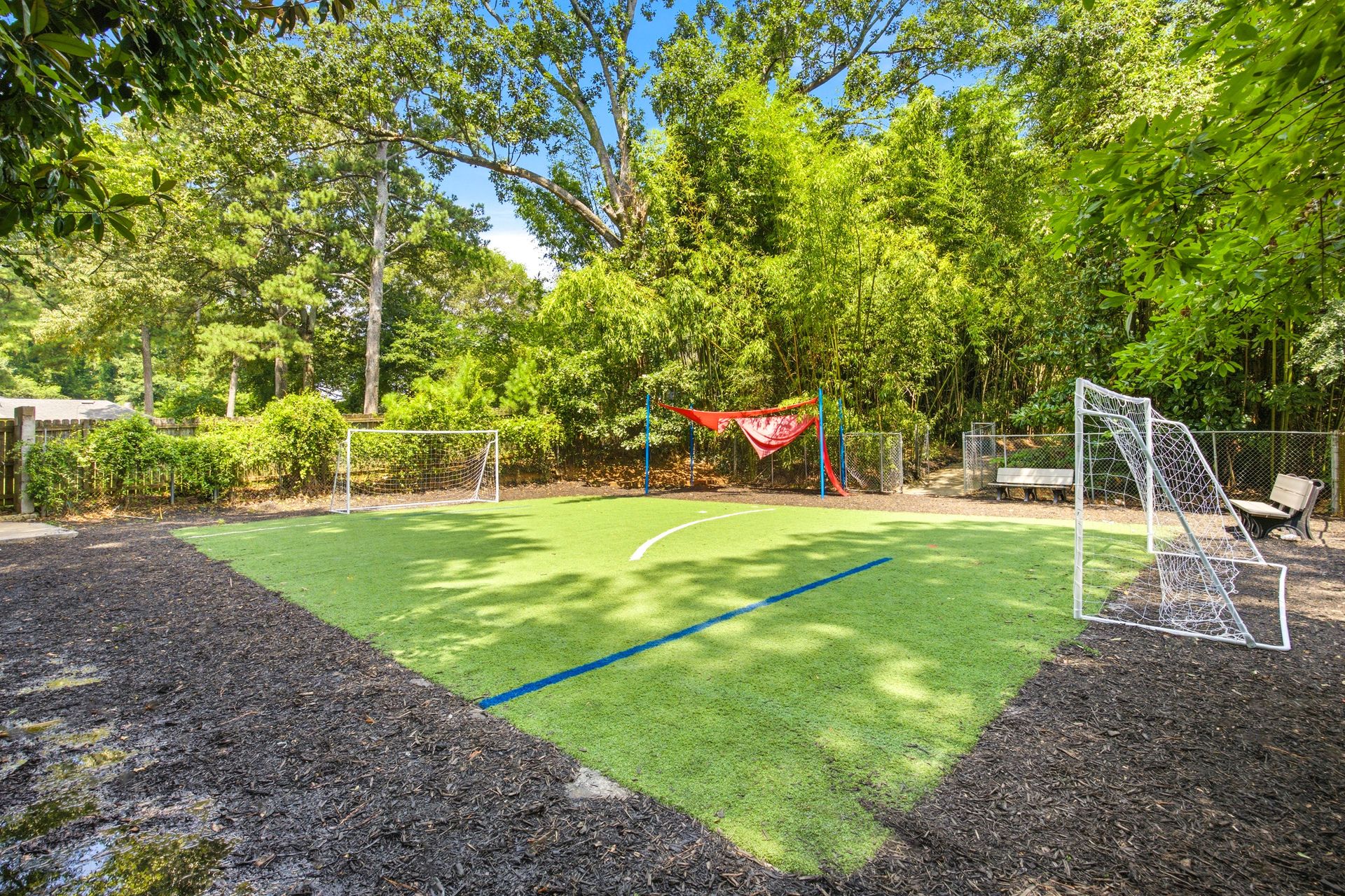 Backyard with artificial turf, a goal net, and trees in bright sunlight