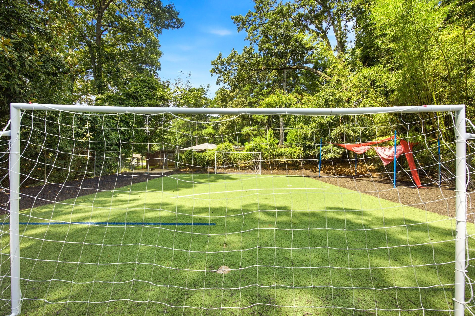 Soccer goal on a sunny grassy field with trees and playground equipment in the background